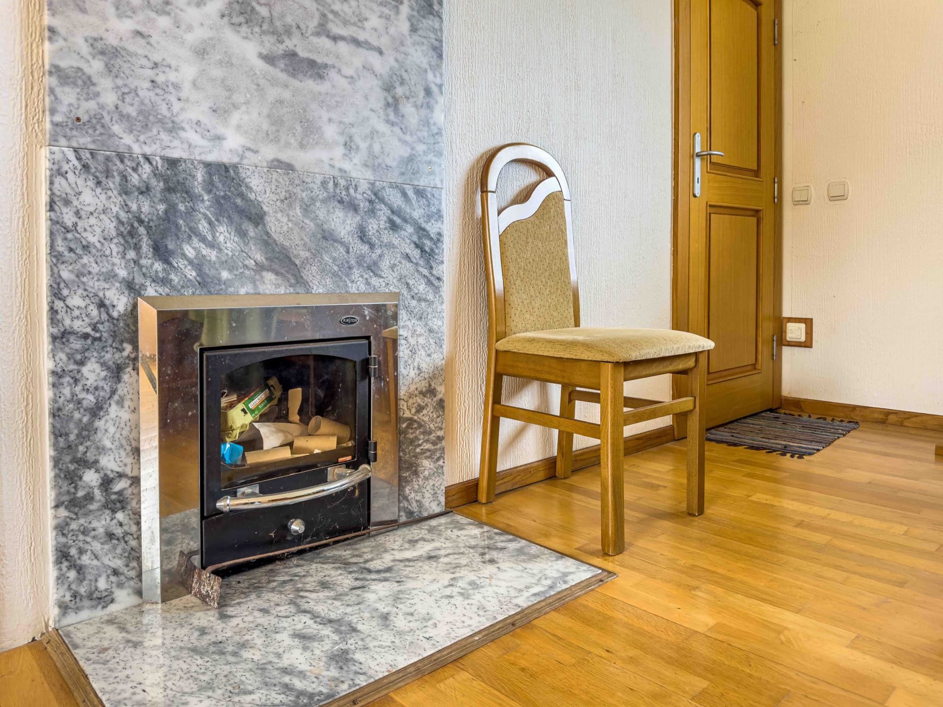Fireplace with gray marble finish and a wooden chair in a house interior in Utjeha, Montenegro.