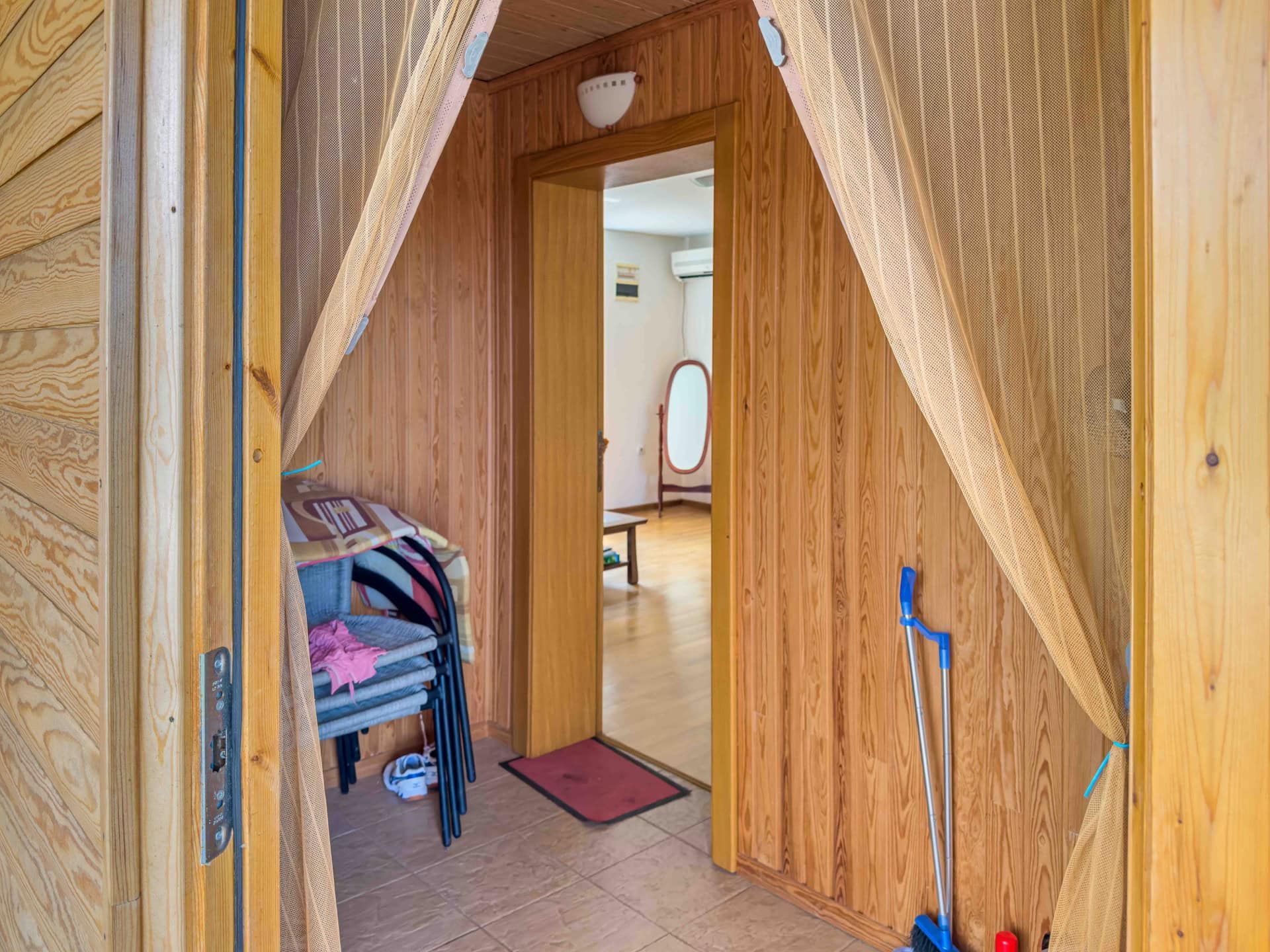 Interior of a house in Uteha, Montenegro: an entryway with wood-paneled walls, tiled floor, and a passage to the living room.