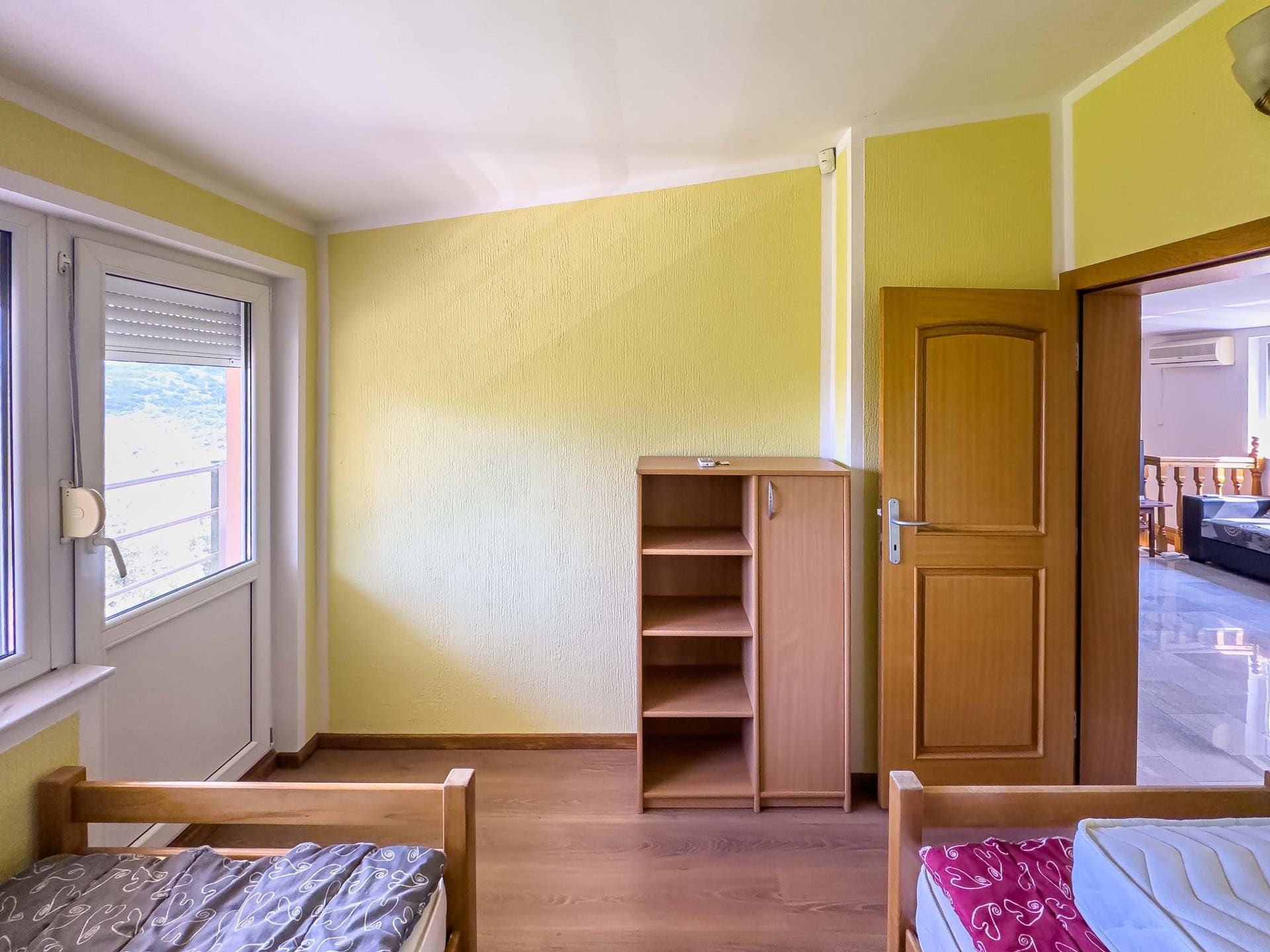 Bedroom in a house in Utjeha, Montenegro: yellow walls, wooden beds, a wardrobe, and access to a balcony with mountain views.