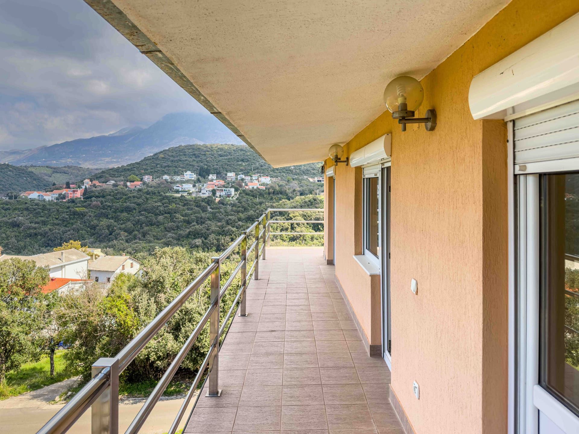 Spacious balcony with tiled floor and mountain views in a house, Uteha, Montenegro. Metal railings and facade.