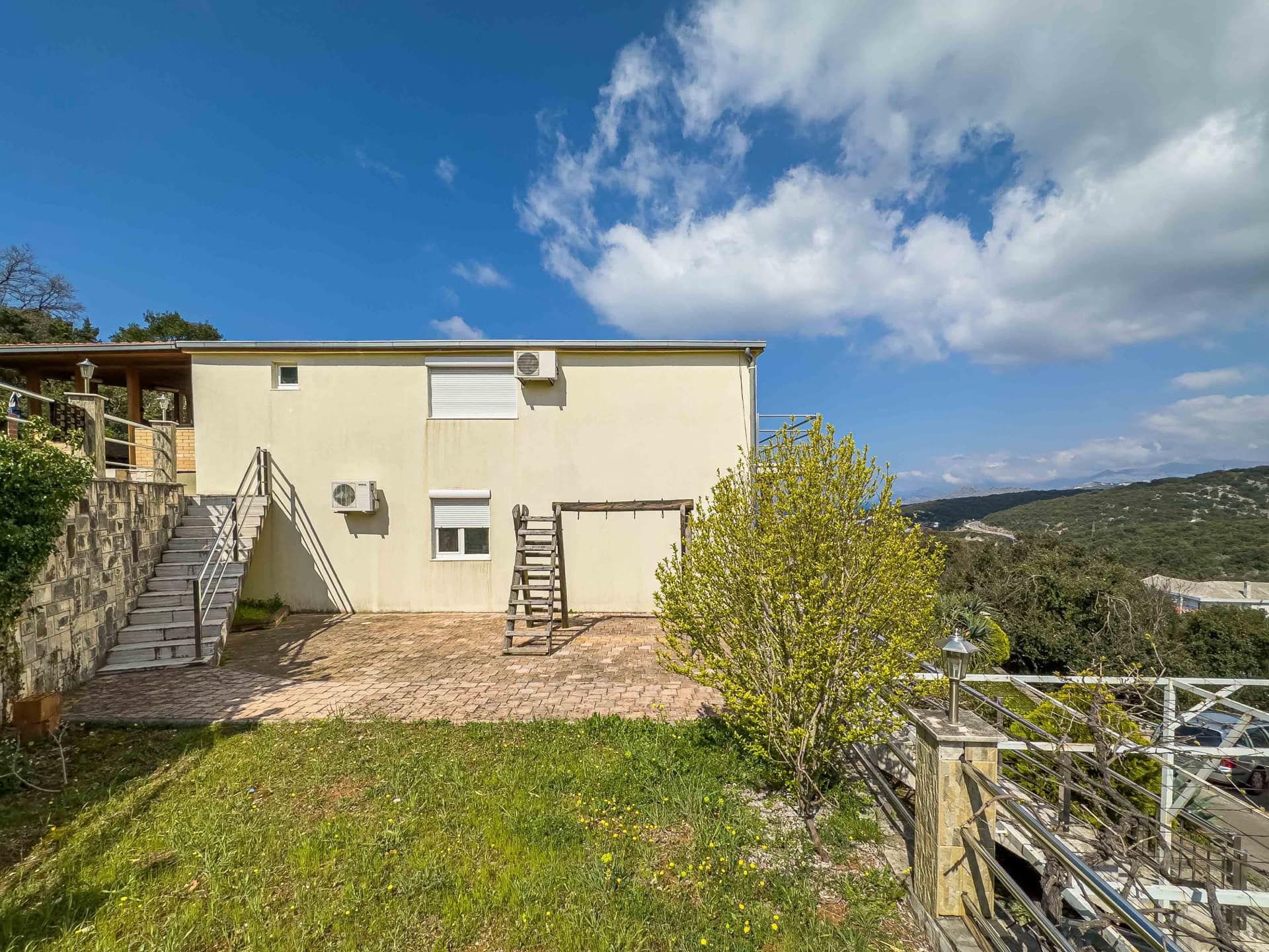 Two-story house with a terrace and mountain views in the village of Uteha, Montenegro: facade, staircase, and surrounding grounds.
