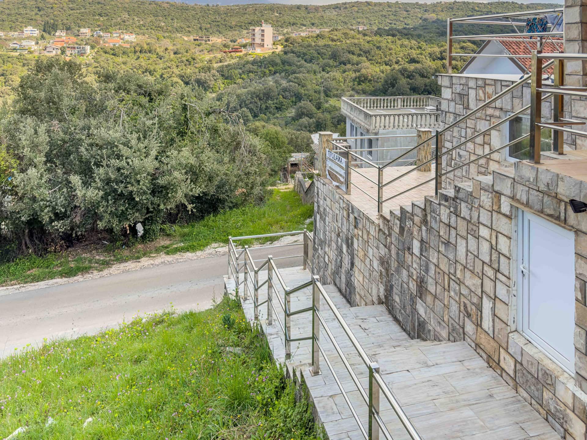 House in Utjeha, Montenegro: stone facade finish, terrace with metal railings, and a view of the hills and road.