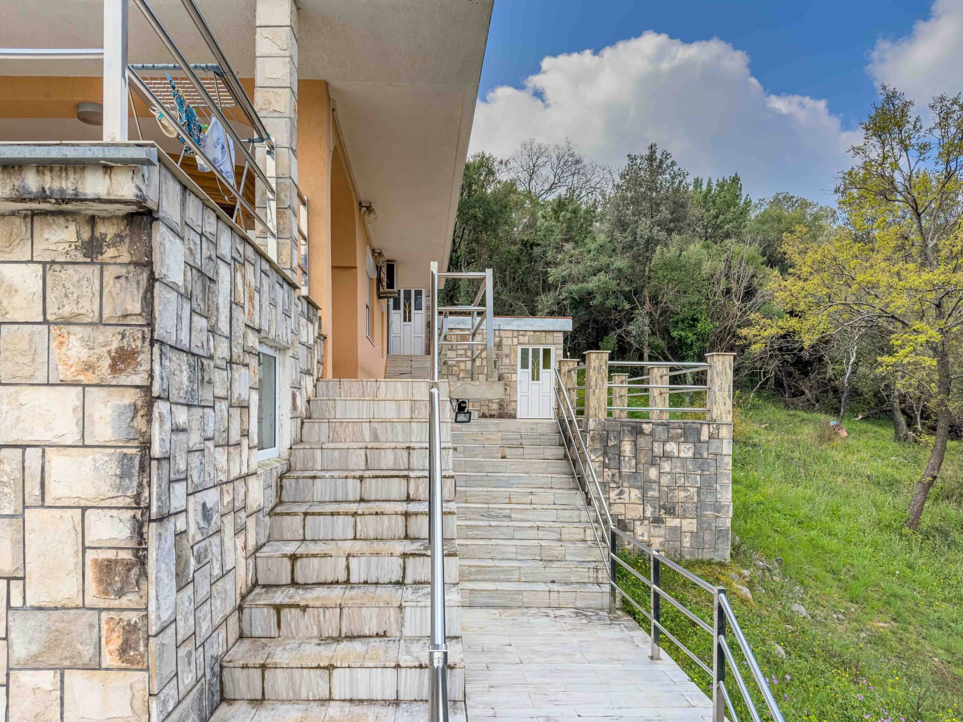 Stone staircase and house terrace in Uteha, Montenegro, overlooking a green garden and metal railing.