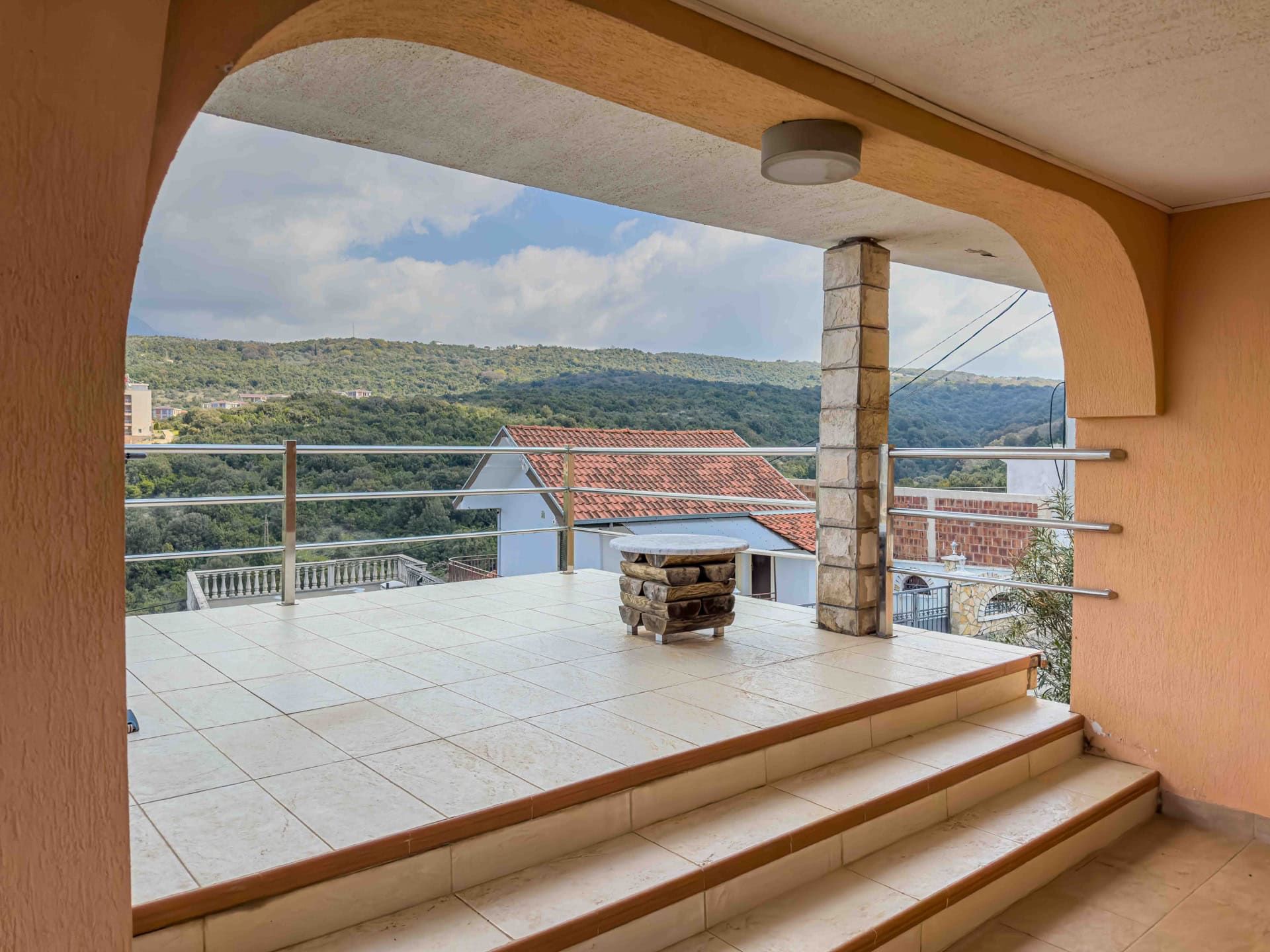 Spacious terrace with mountain views in a house, Uteha, Montenegro: tiled floor, stone column, and stainless steel railings.