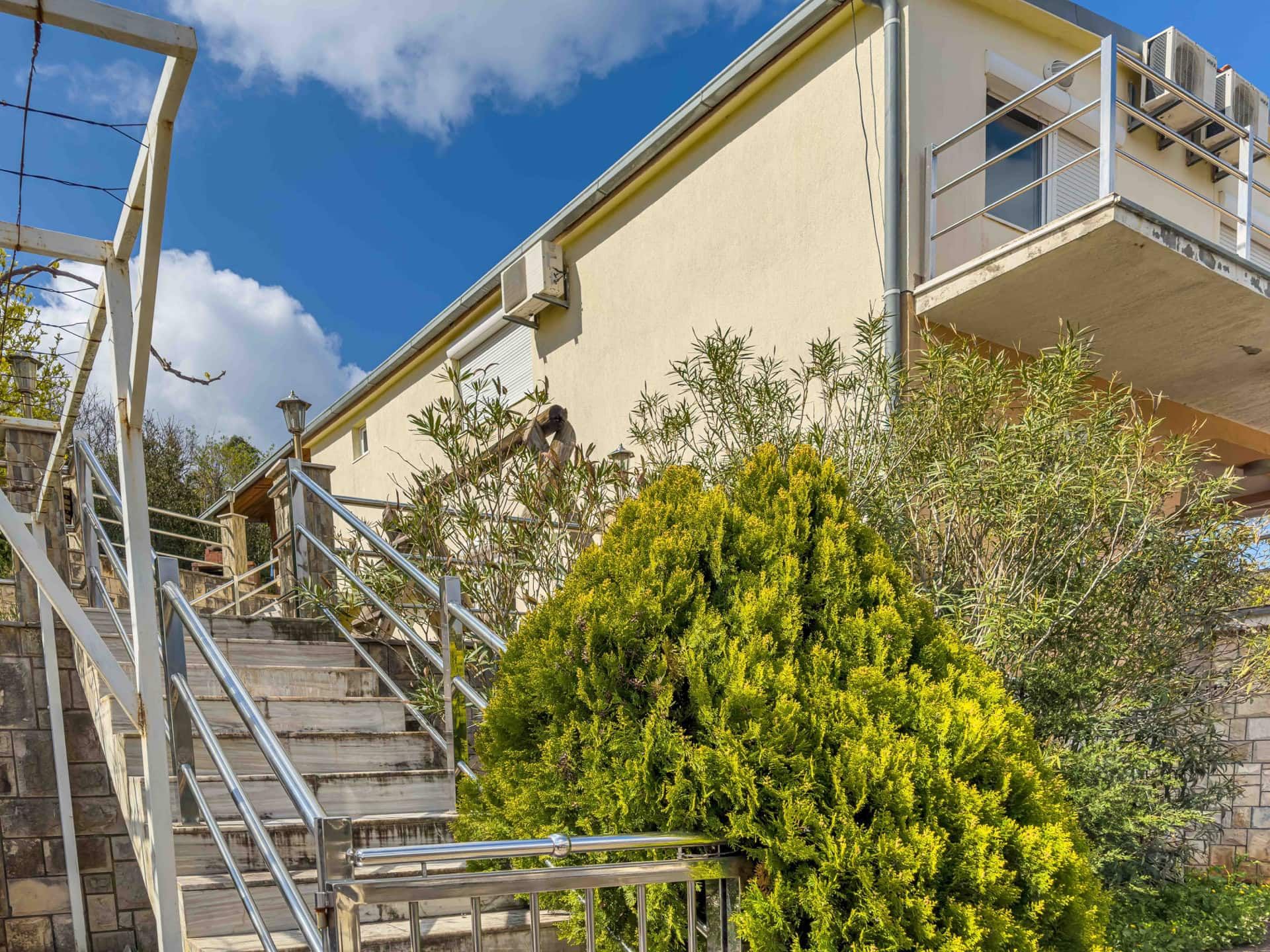 House facade in Uteha, Montenegro: a stone staircase with stainless steel railings and a well-kept garden at the entrance.