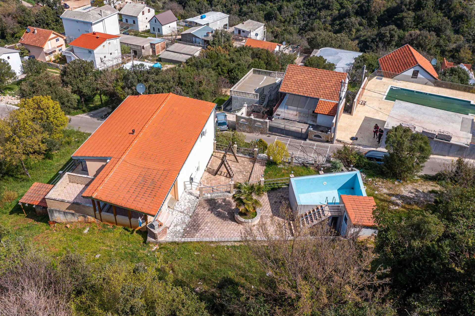 Aerial view of a house in Utjeha, Montenegro: a plot with a pool, terrace, parking, and a tiled roof.