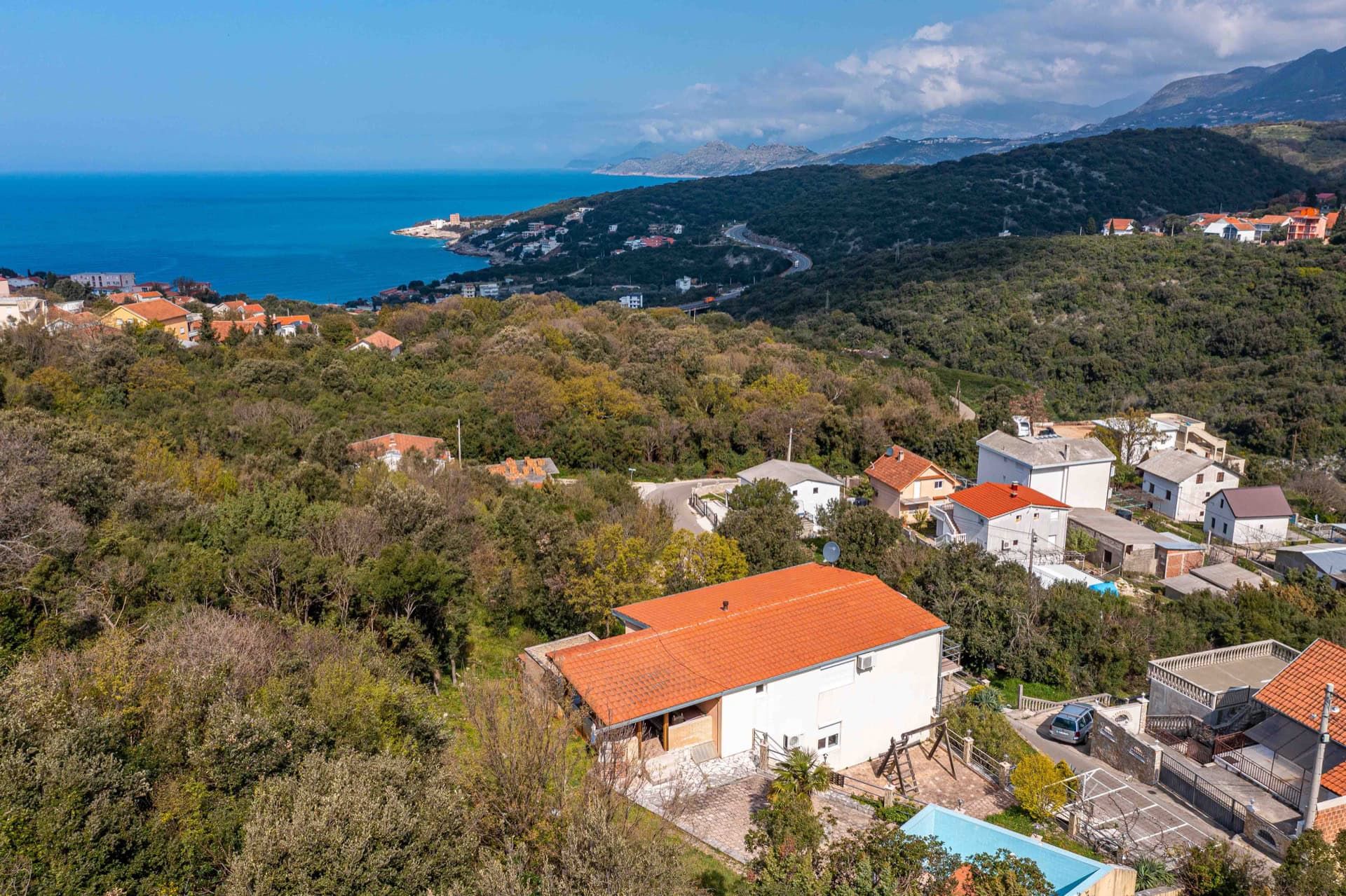 Aerial view of a house with a pool in Utjeha, Montenegro: panorama of the sea, mountains, and green landscape around the property.