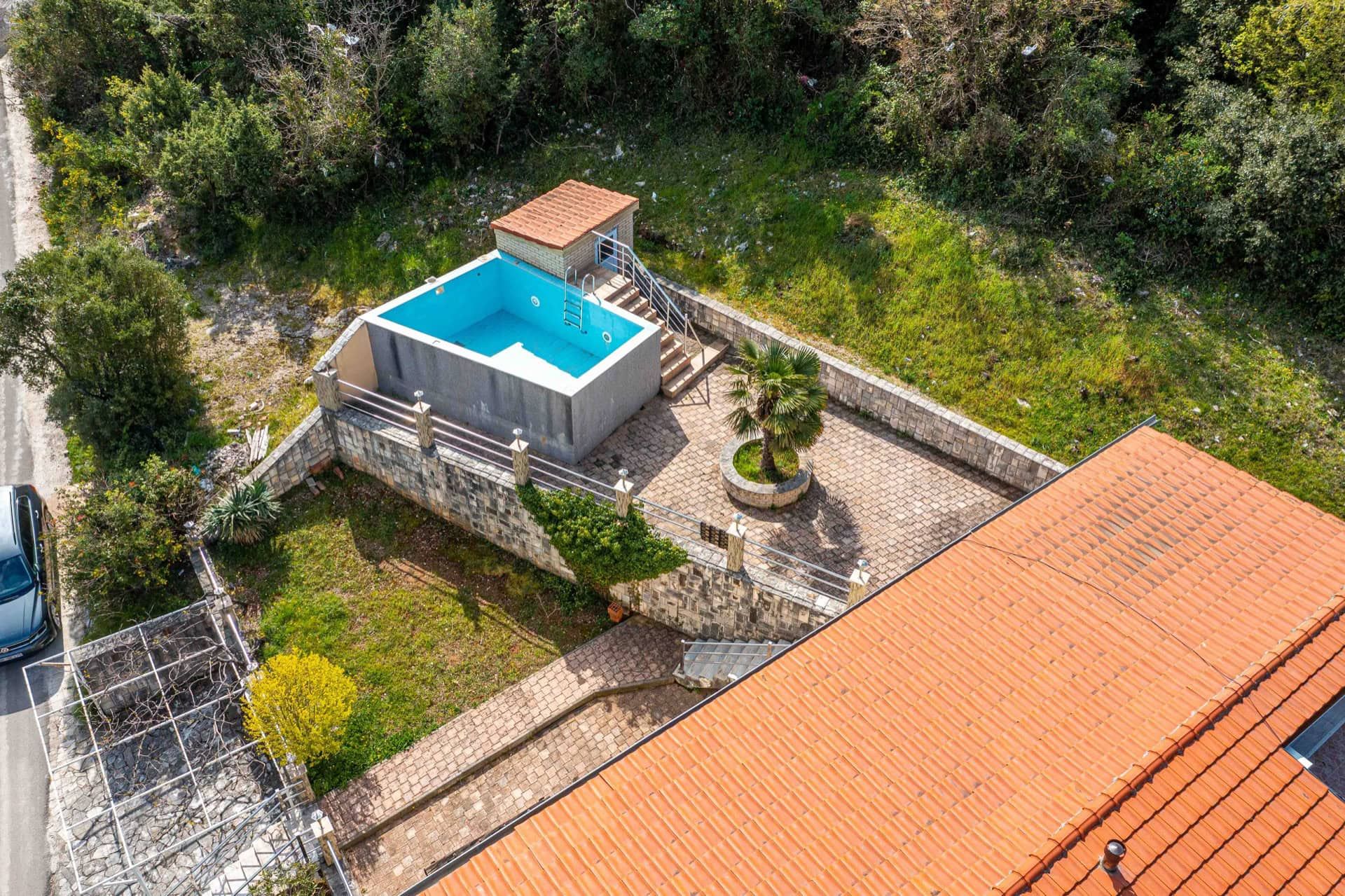 Top view of a private house with a pool and terrace in Utjeha, Montenegro: stone finish, a palm tree, and a green garden.