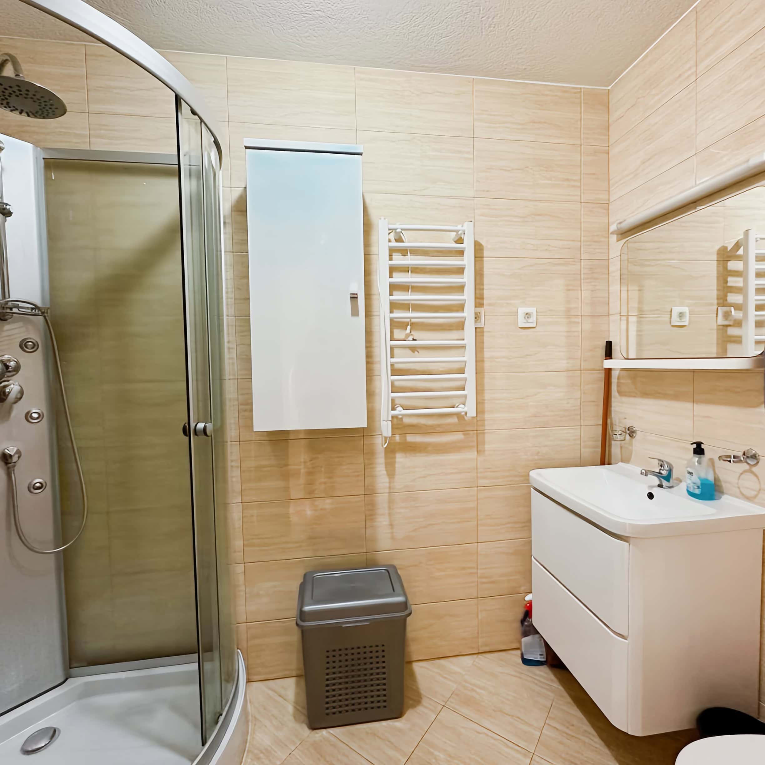 Bathroom in an apartment in Bečići, Montenegro: shower cabin, white vanity with sink, and towel warmer.