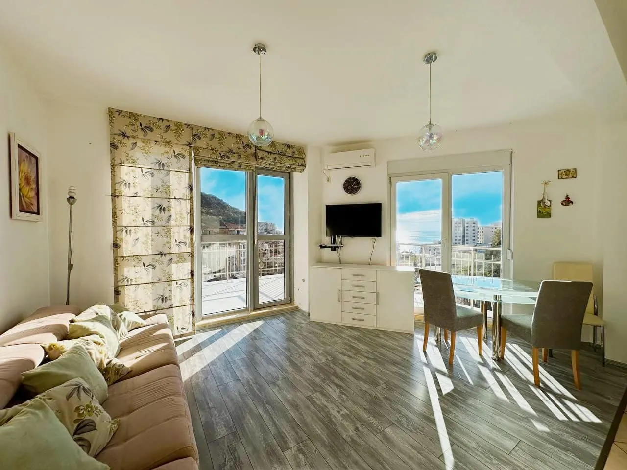 Living room with sofa, glass dining table, TV, and balcony doors overlooking the sea.