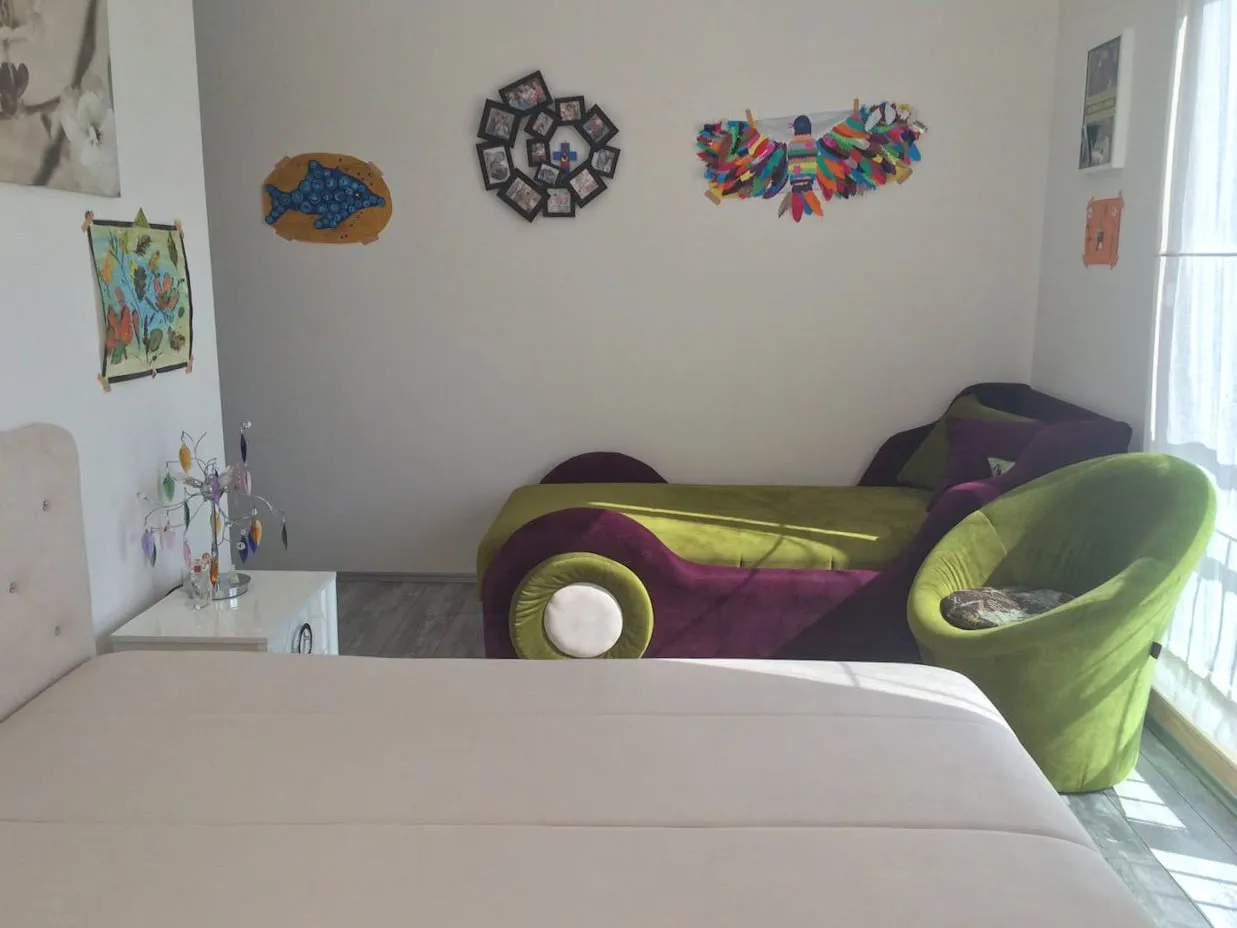 Bedroom featuring a white bed, a colorful car-shaped sofa, and children's artwork on the wall.