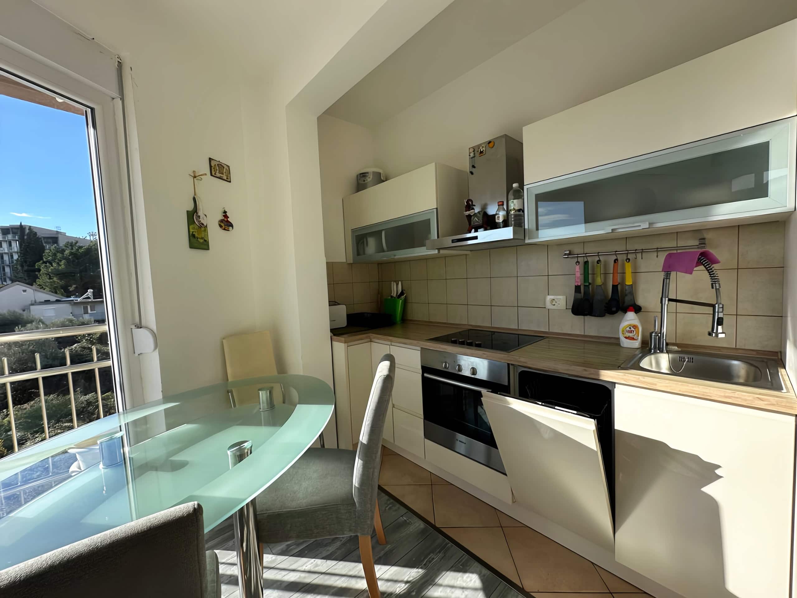 Bright kitchen in an apartment in Bečići, Montenegro: glass table, built-in appliances, and a mountain view from the window.