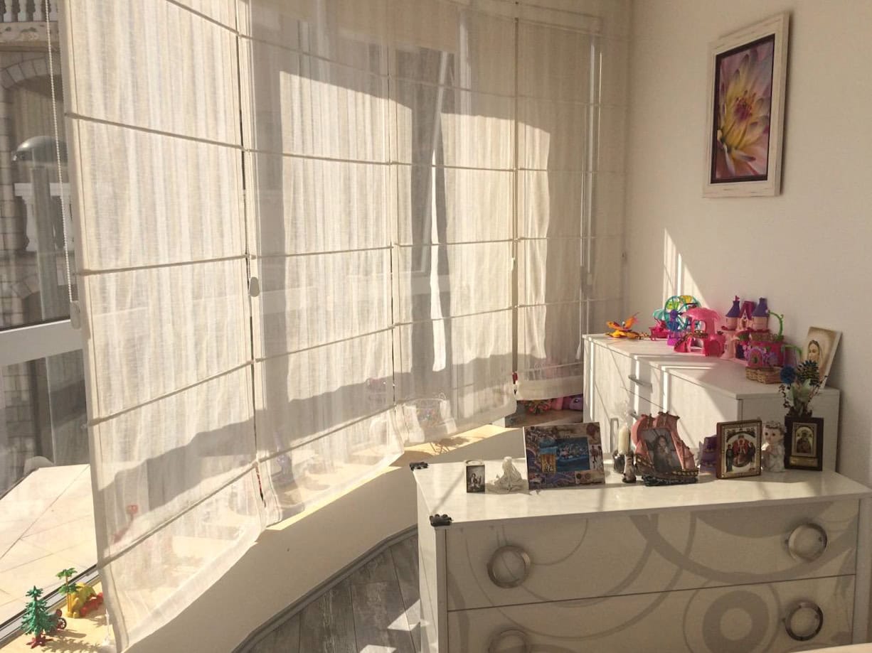 Bright bedroom in an apartment in Bečići, Montenegro: white furniture, Roman shades on the windows, and decorative interior accents.