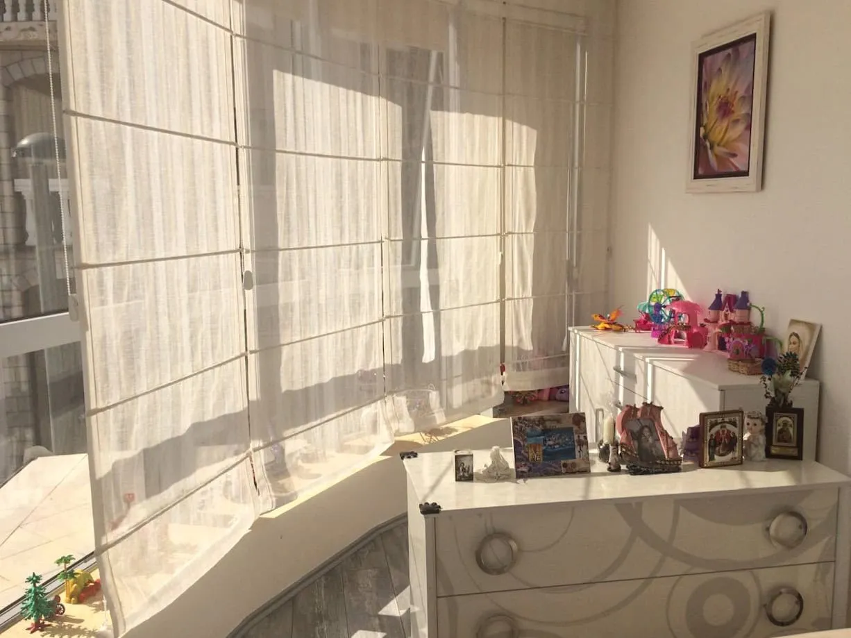 Bright room with a white dresser, toys, and photos near a glassed-in balcony area.