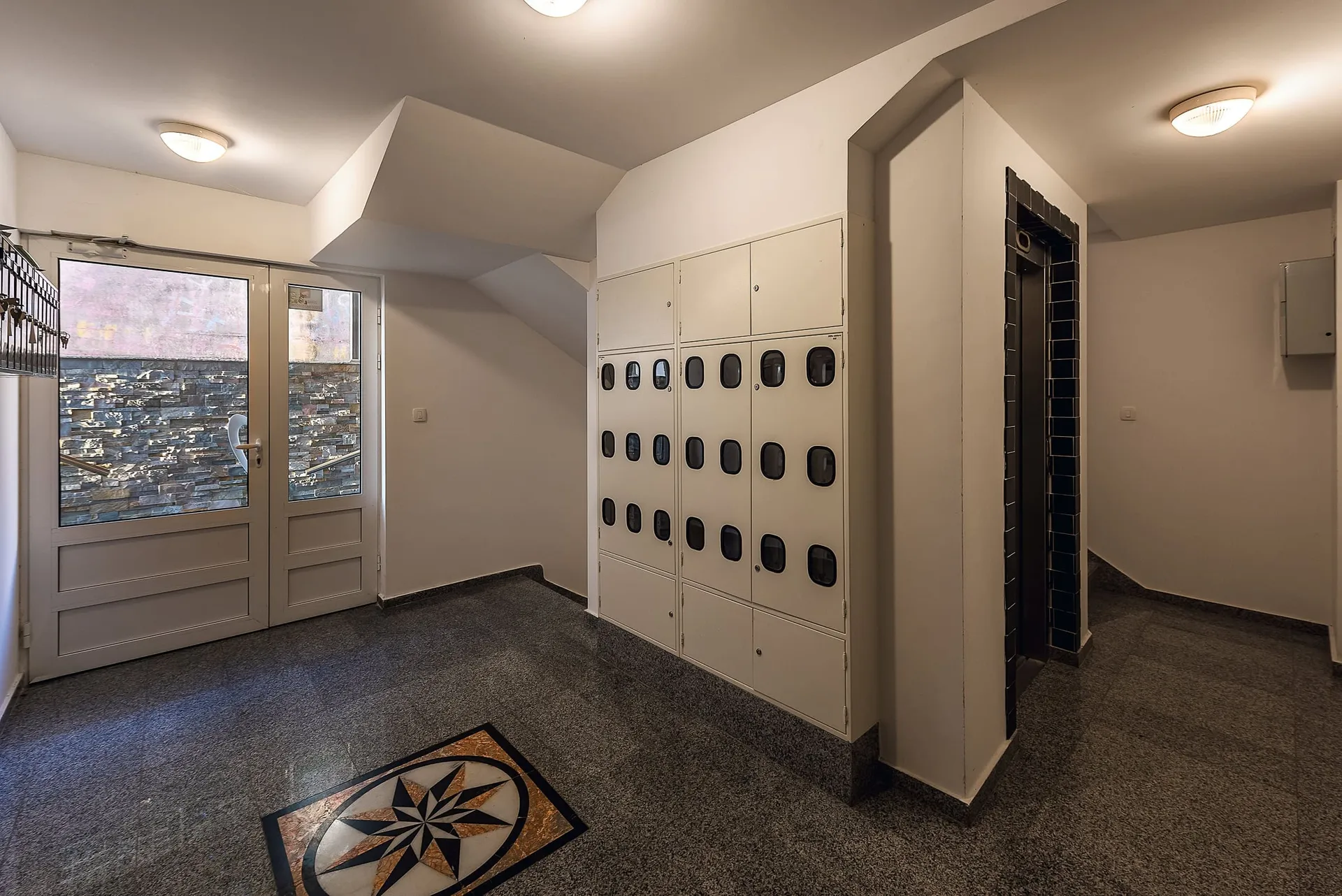 Building entrance hall featuring mailboxes, an elevator, and a decorative floor mosaic.