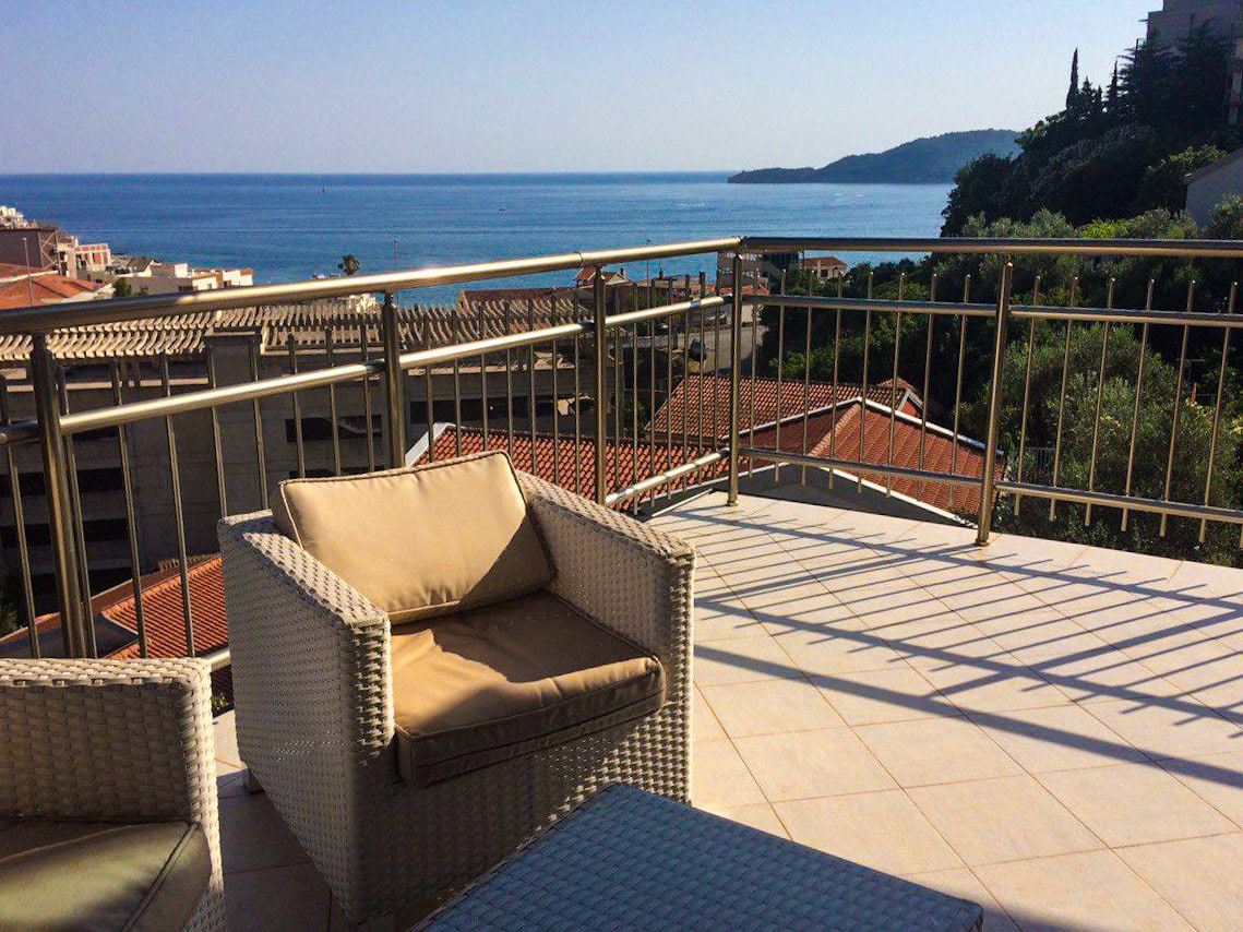 Terrace with wicker furniture and panoramic sea view in an apartment in Bečići, Montenegro.