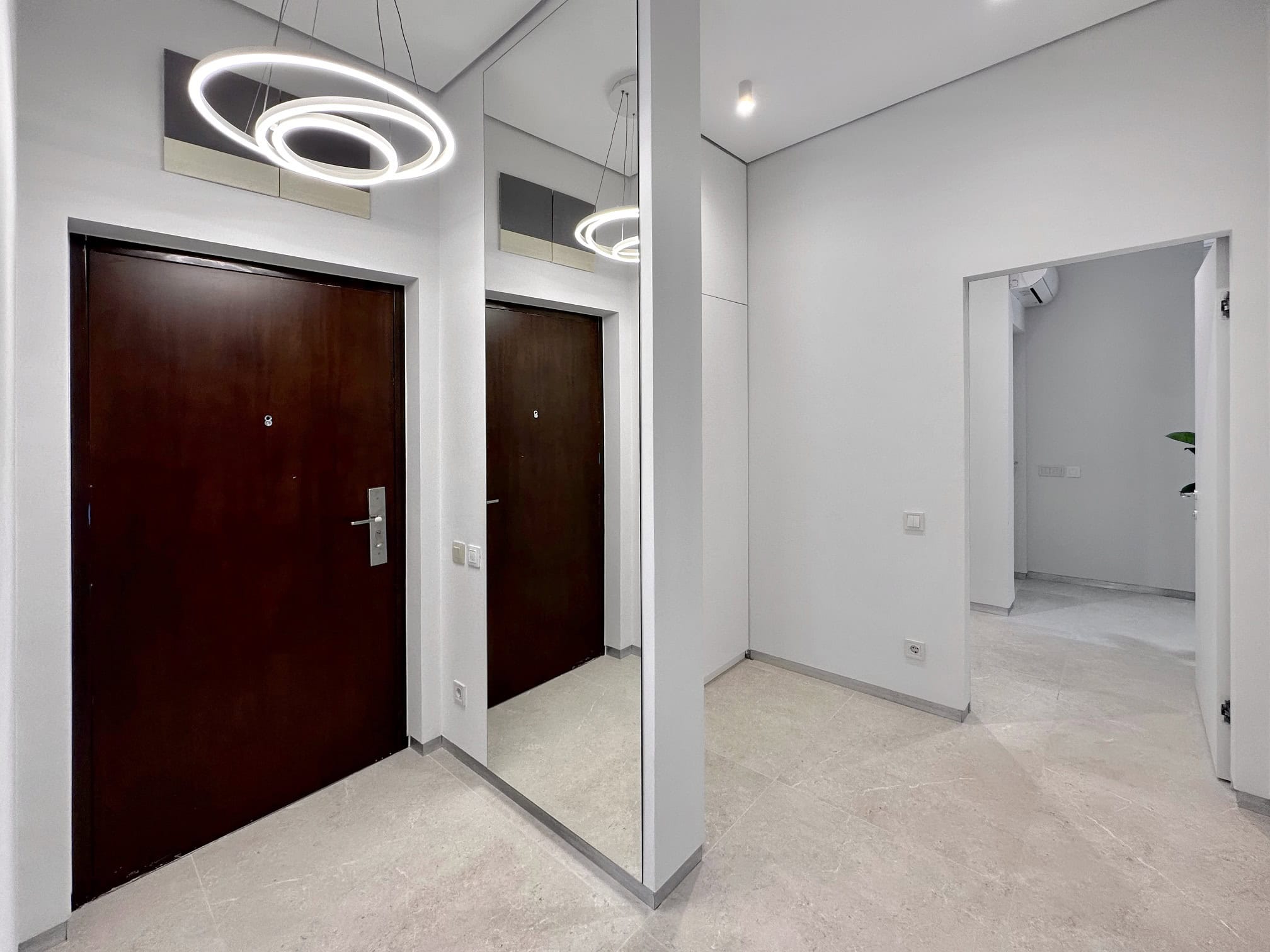 Modern hallway in an apartment, Bečići, Montenegro: light-toned finishes, large mirror, and designer chandelier.