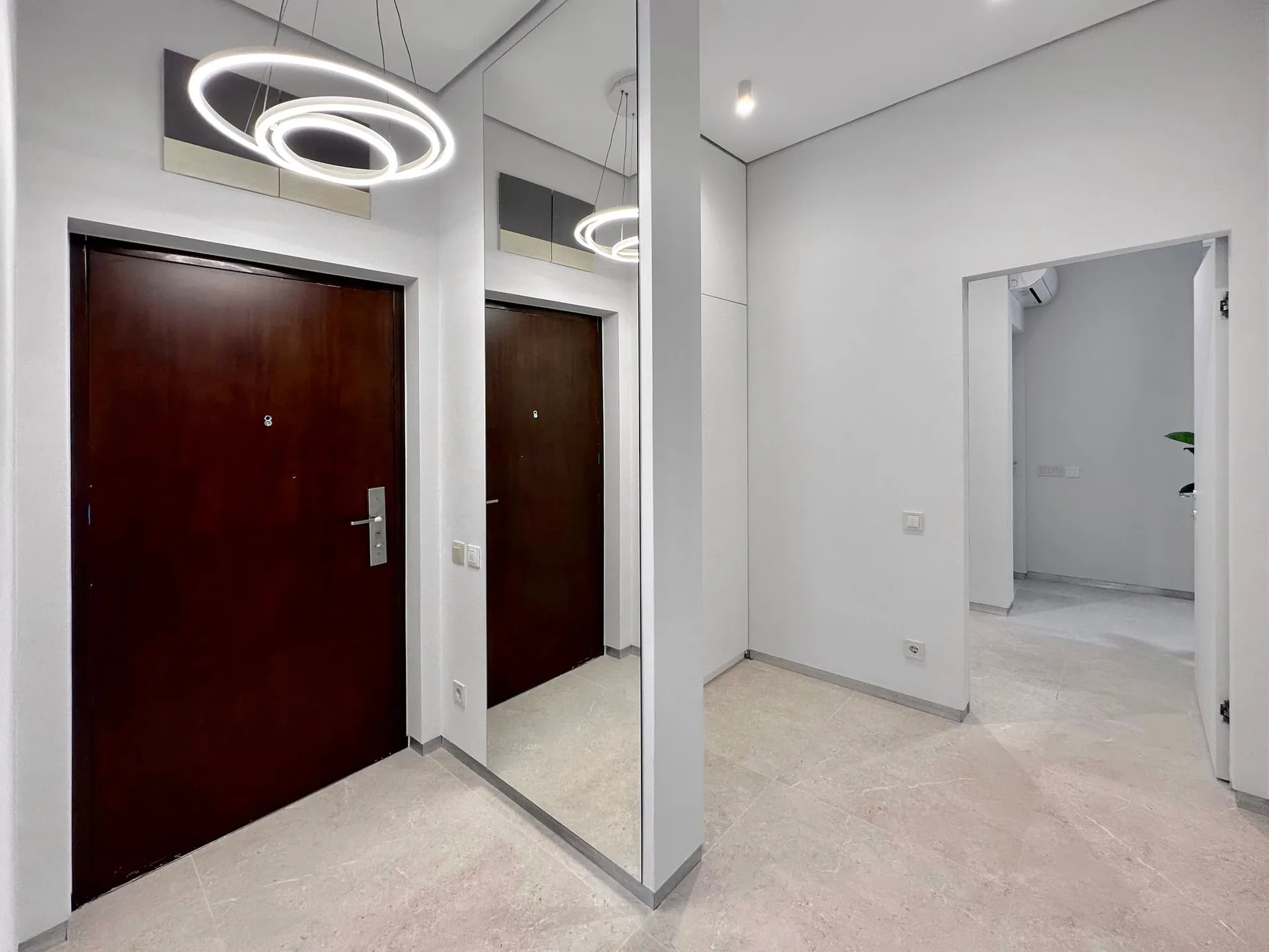 Modern entryway featuring a dark wooden door, a large floor mirror, and ring pendant lights over tiled flooring.