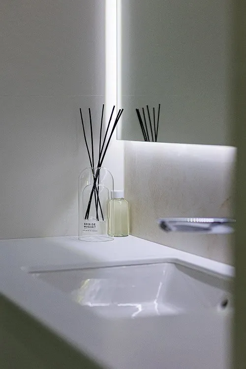 White sink, backlit mirror, and reed diffuser on the bathroom vanity counter.