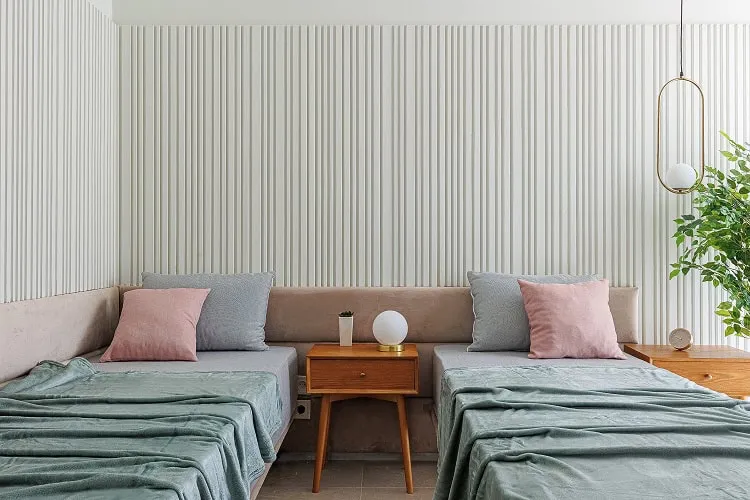 Two single beds with pillows and a wooden nightstand between them against a striped wall.