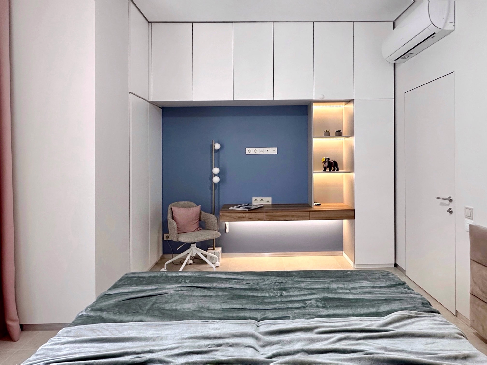 Modern bedroom in an apartment in Bečići, Montenegro: built-in wardrobe, workspace with lighting, and a bed.