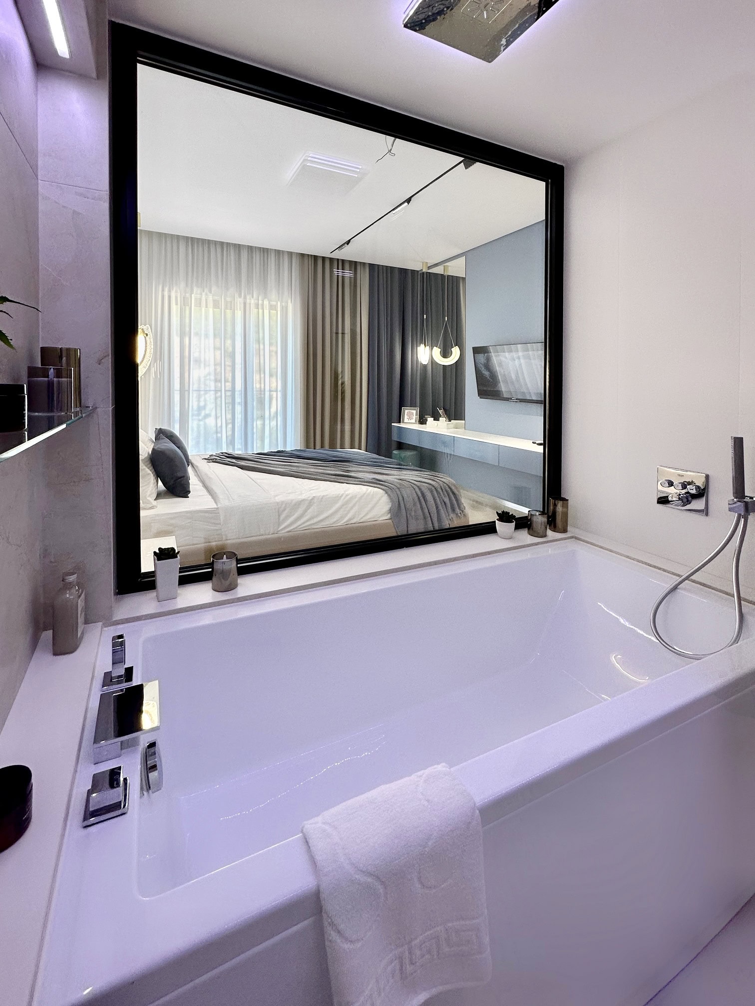 Modern bathroom with a panoramic window looking into the bedroom in an apartment in Becici, Montenegro. White bathtub, stylish interior.