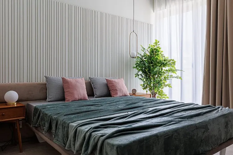 Modern bedroom featuring a double bed with pink and gray pillows, wooden nightstand, green plant near window, and vertical slat wall paneling.