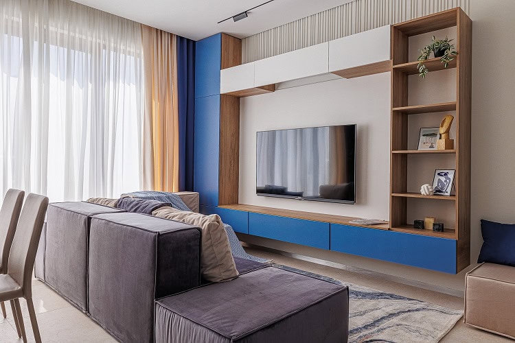 Modern living room in an apartment in Bečići, Montenegro: modular sofa, TV area with blue facades, and panoramic windows.