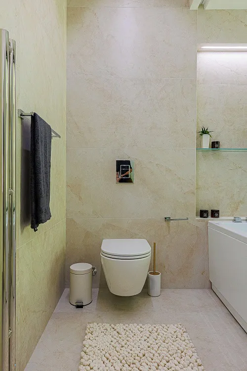 Modern bathroom featuring a wall-mounted toilet, glass shower enclosure, and beige marble tiles.