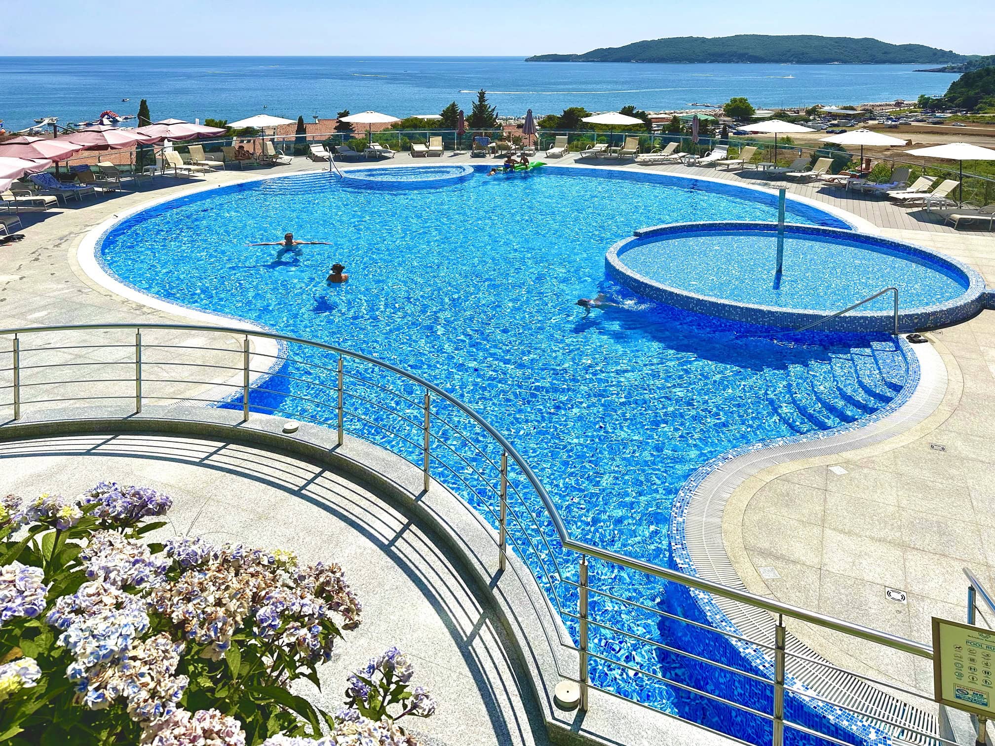 Outdoor swimming pool with a sea view in a residential complex in Becici, Montenegro: relaxation area with sun loungers and a terrace.