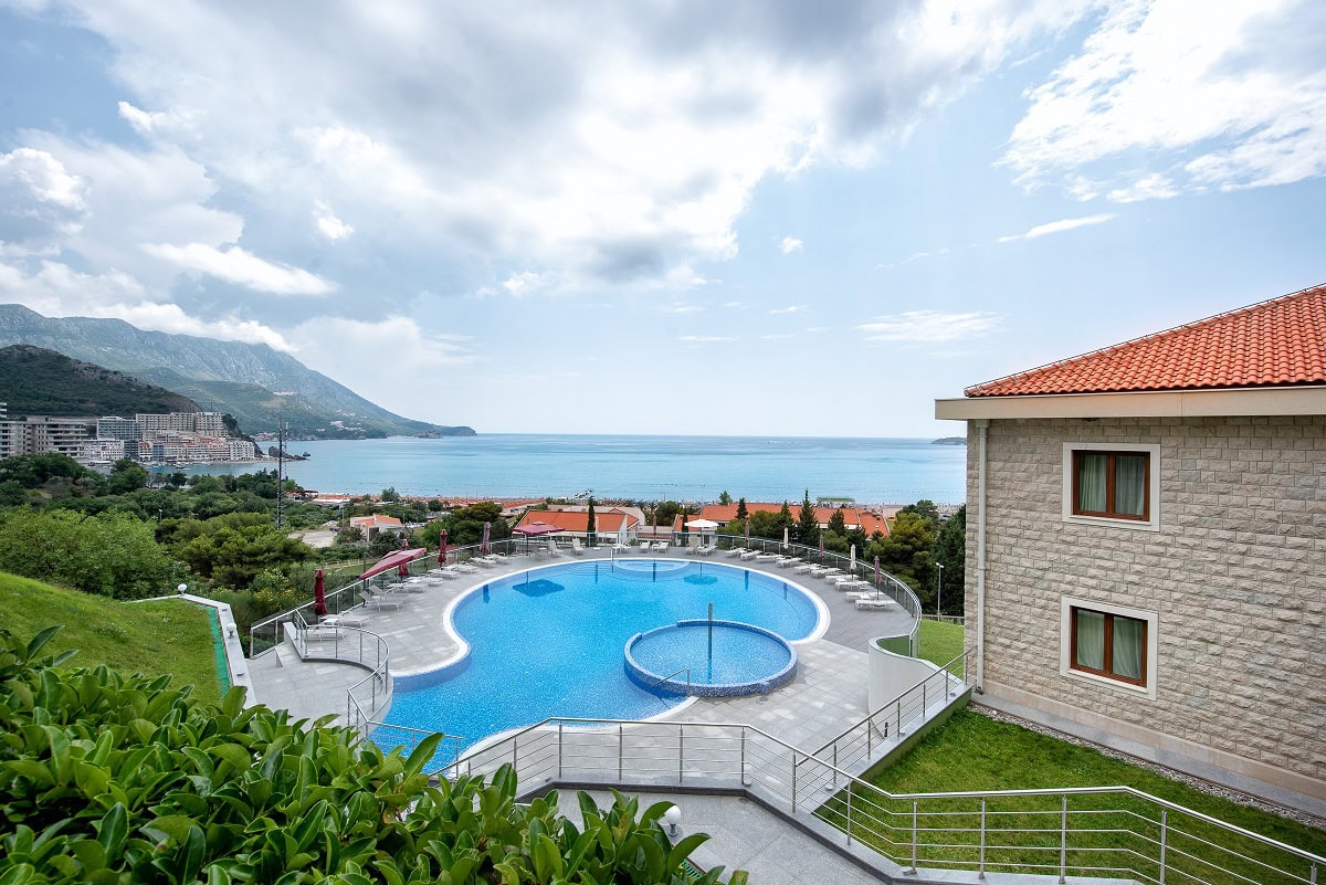 Outdoor swimming pool with a sea and mountain view at a residential complex in Becici, Montenegro: lounge area with sun loungers and a terrace.