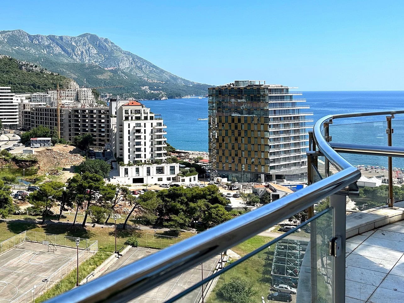 View from the apartment balcony in Bečići, Montenegro: a panorama of the sea, mountains, and the resort's modern residential complexes.