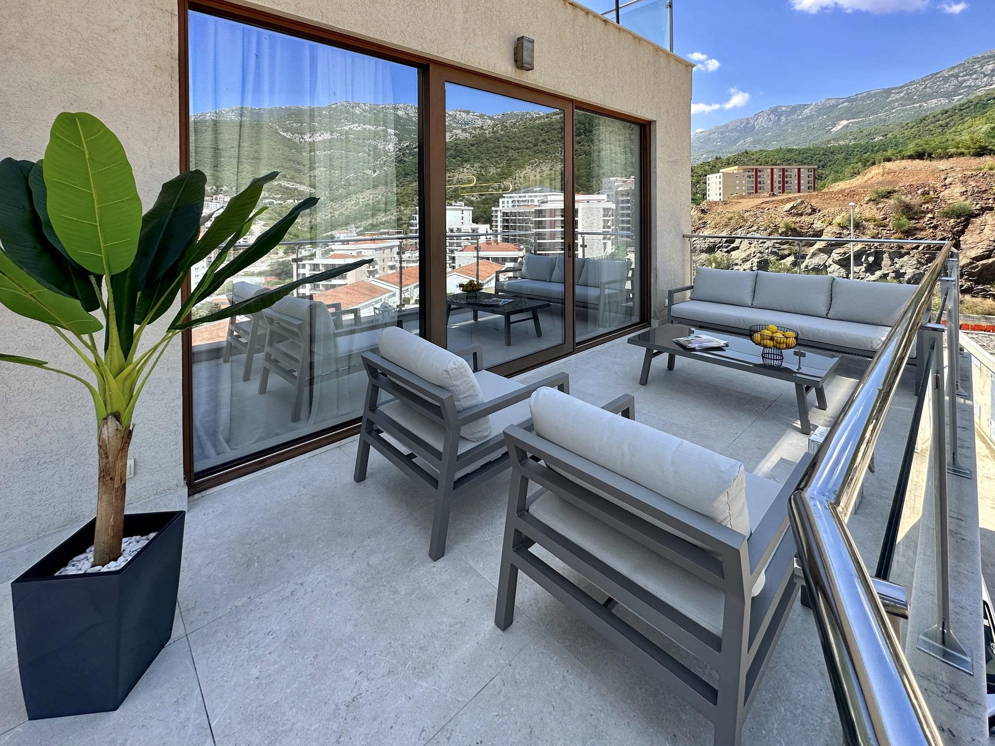 Spacious terrace with furniture and mountain views in a Becici apartment, Montenegro. Modern balcony with panoramic windows.
