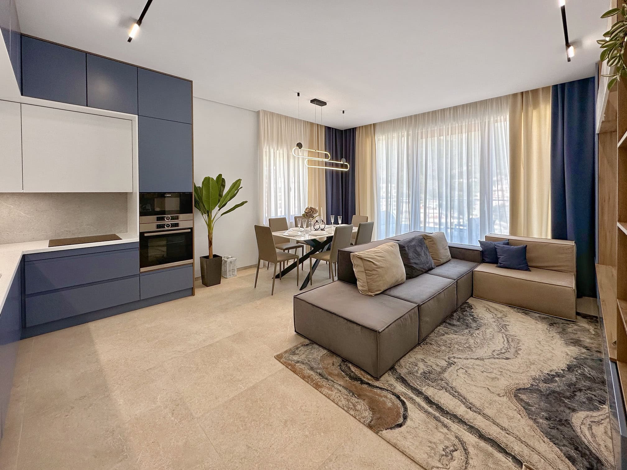 Modern living room with kitchen in an apartment in Bečići, Montenegro: stylish furniture, dining area, and panoramic windows.