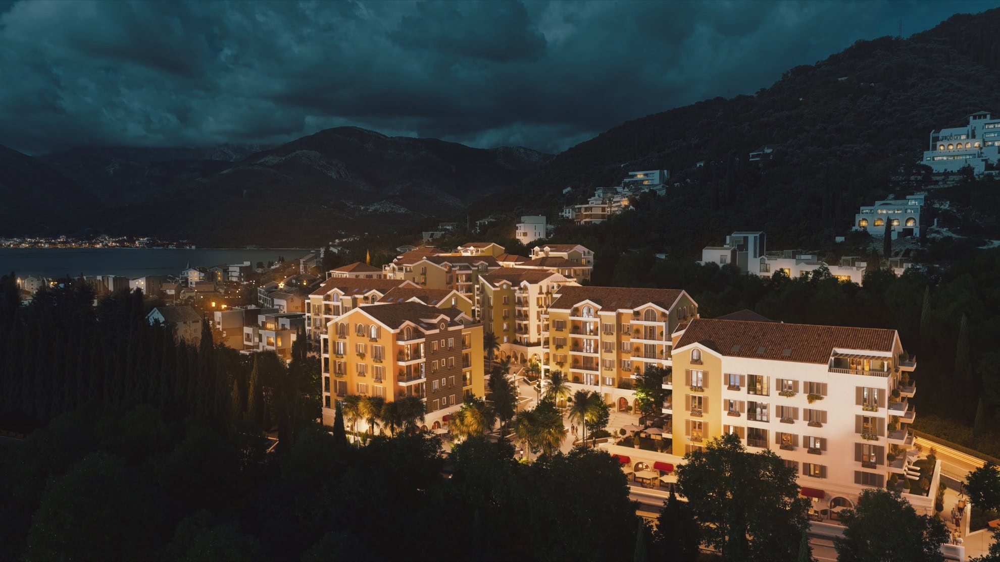 Evening view of a residential complex in Tivat, Montenegro: modern buildings with exterior lighting, terraces, and views of the mountains and the sea.