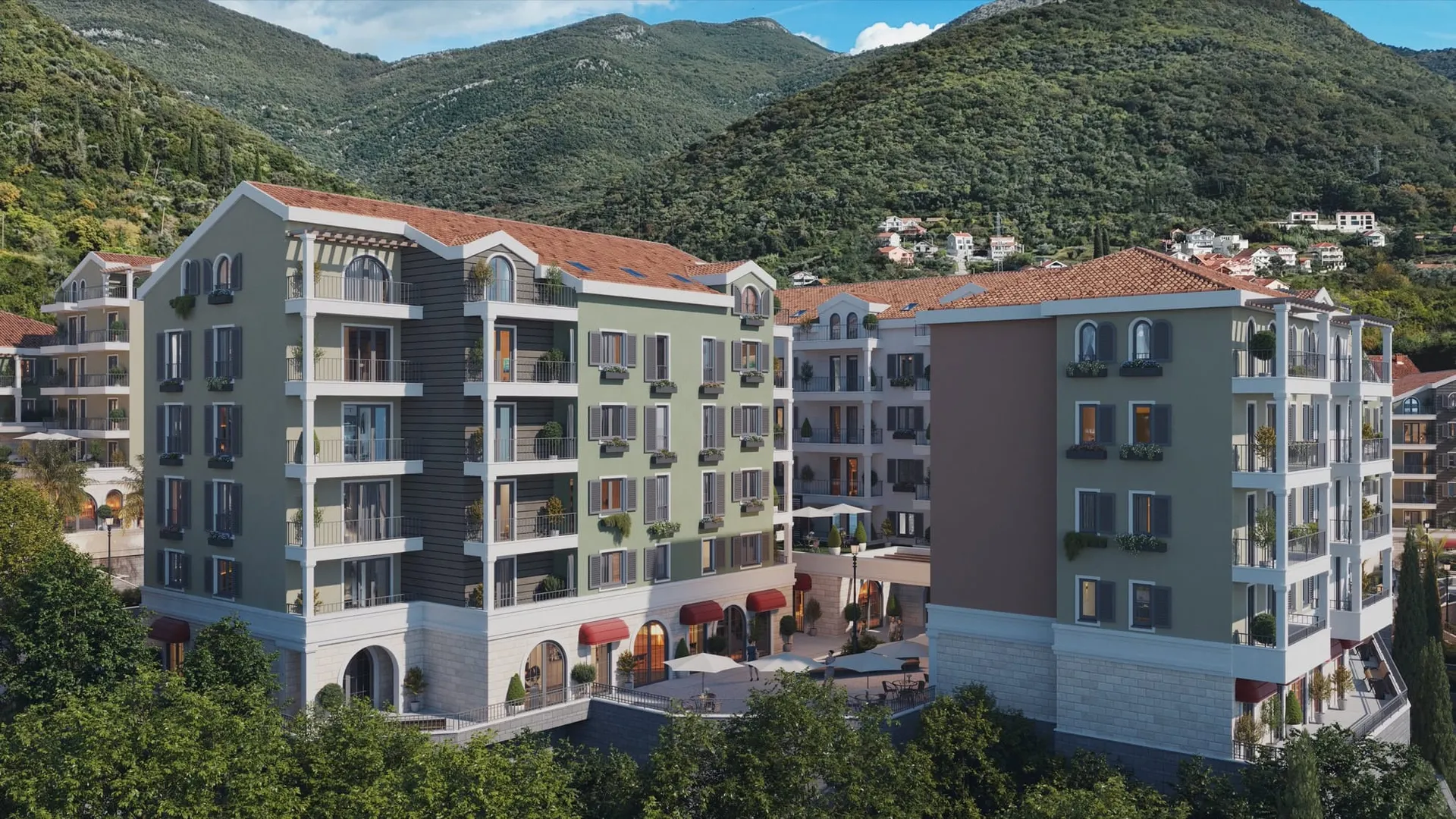 Exterior view of a multi-story residential complex with balconies and red tile roofs against green mountains.