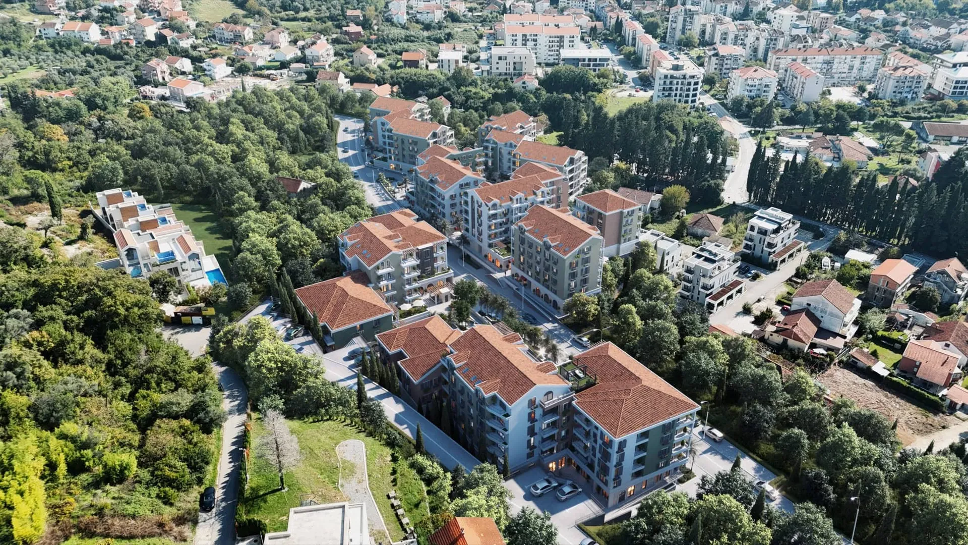 Aerial view of a residential area featuring multi-story buildings with red roofs surrounded by dense trees.