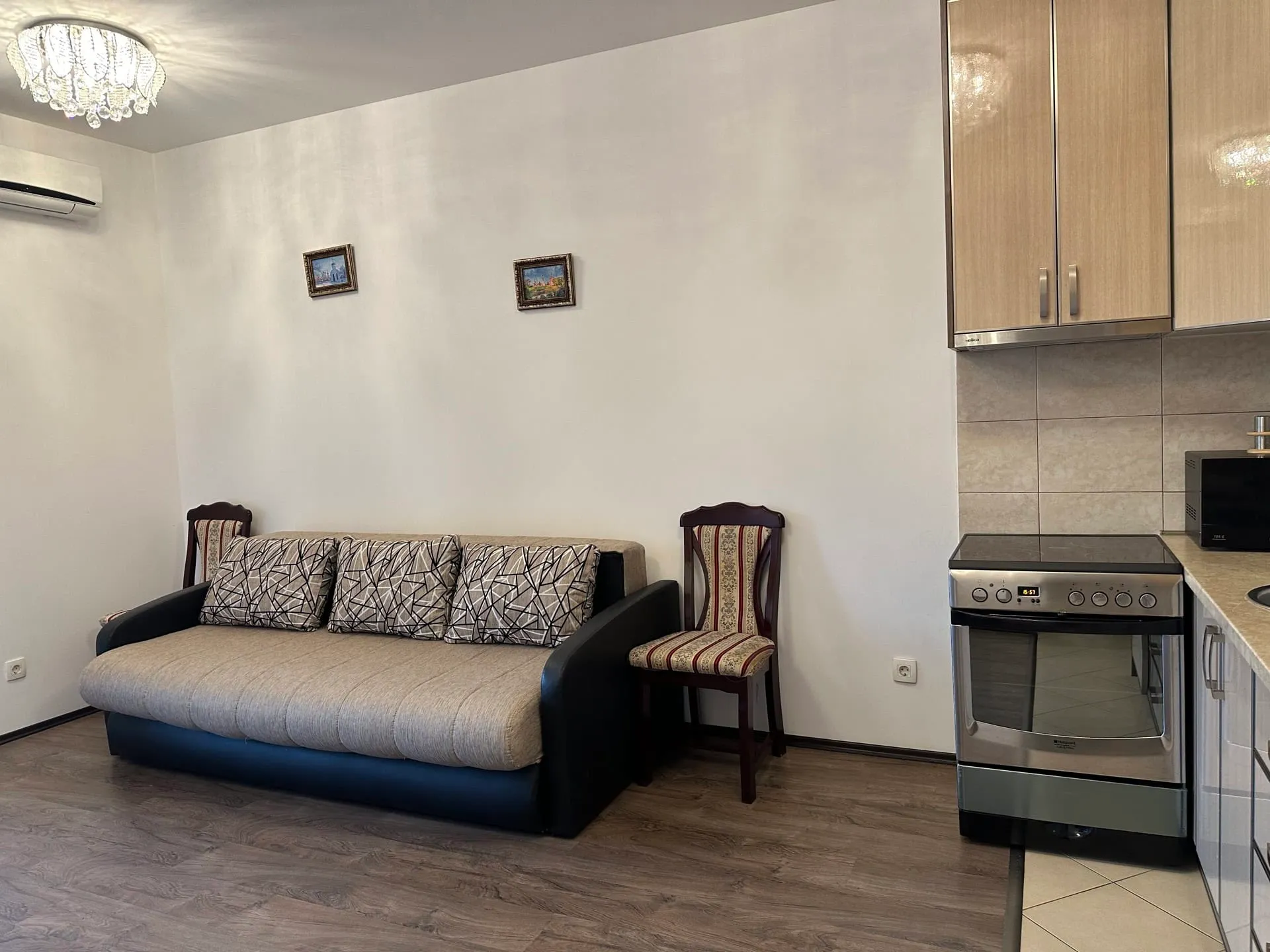 Living area with a sofa and chair adjacent to kitchen cabinets and an oven.