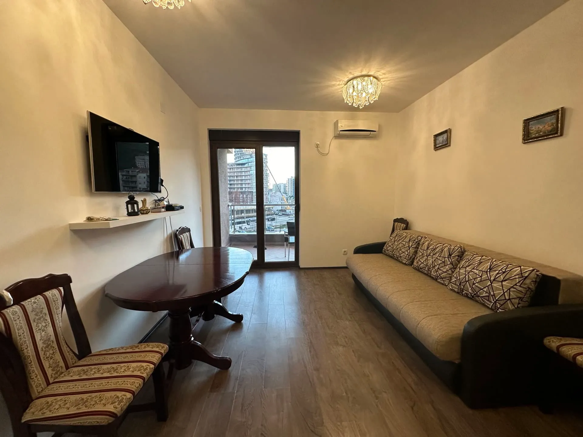 Living room featuring a sofa, dining table, wall-mounted TV, and glass door leading to a balcony.