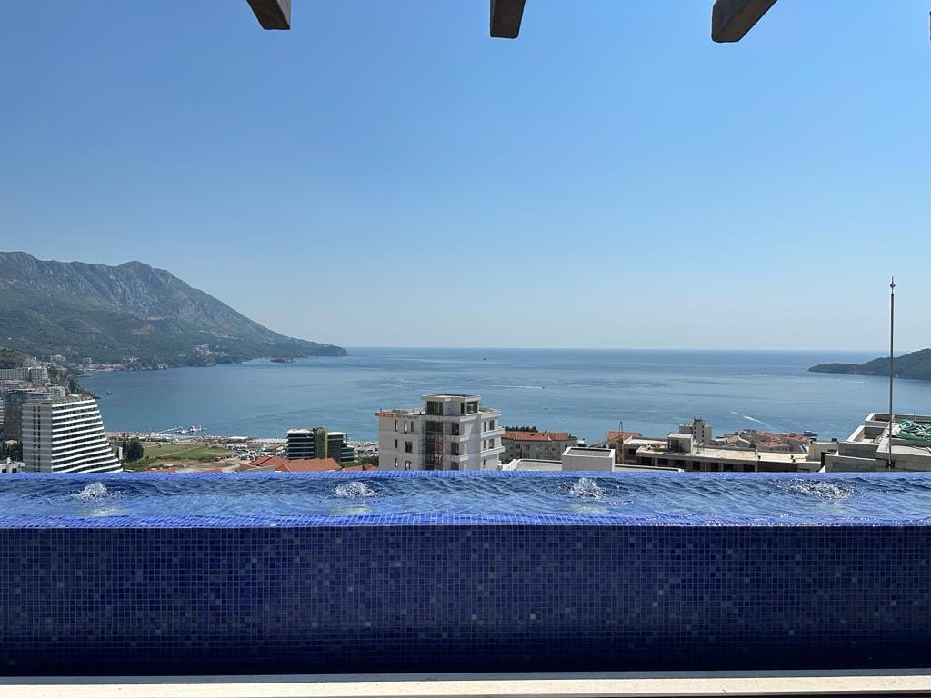 Panoramic view of the sea and mountains from the penthouse pool in Bečići, Montenegro, with a terrace and blue mosaic finish.