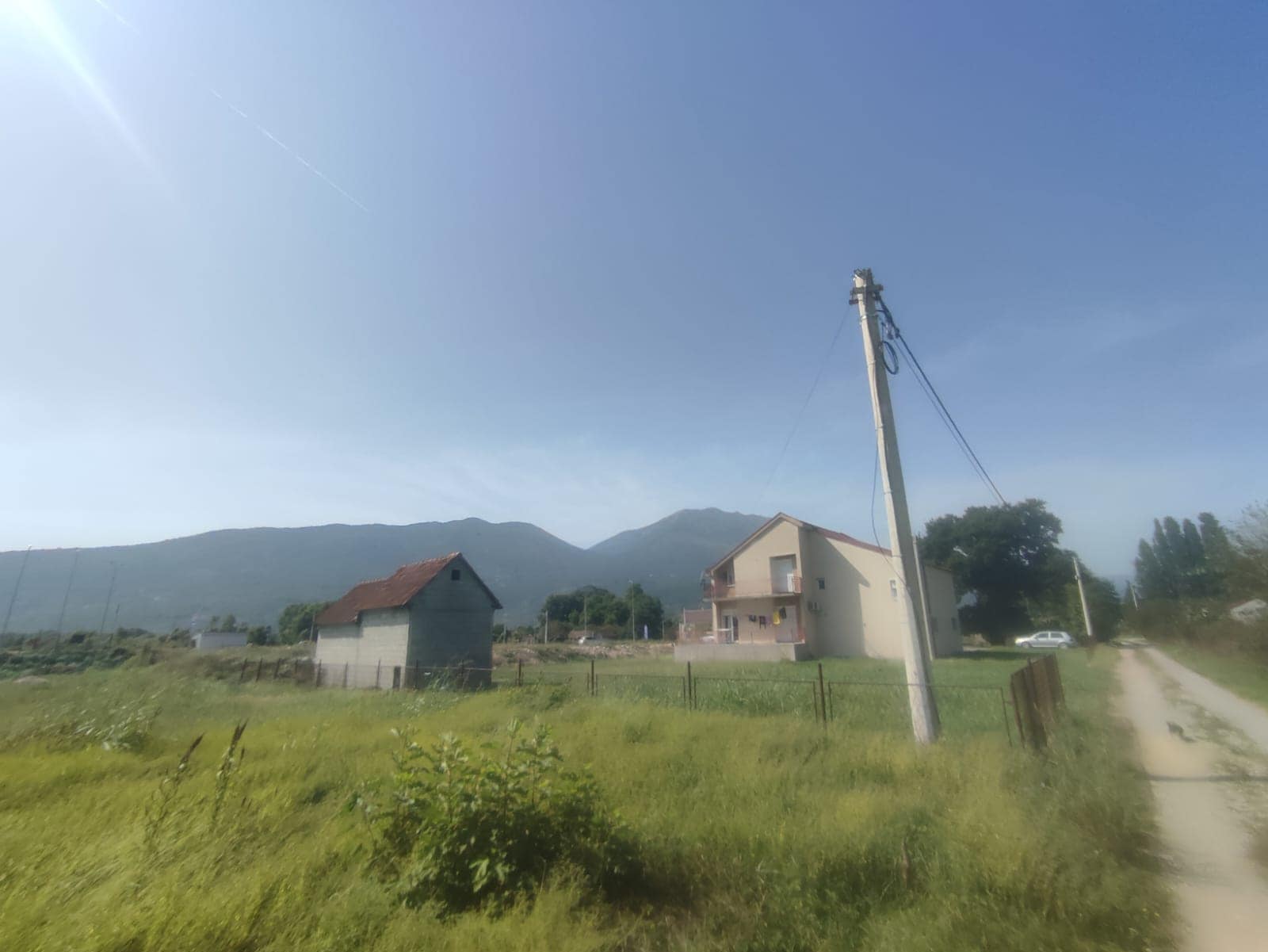 Two-story house with a plot and mountain views in Danilovgrad, Montenegro, against a backdrop of countryside and a road.