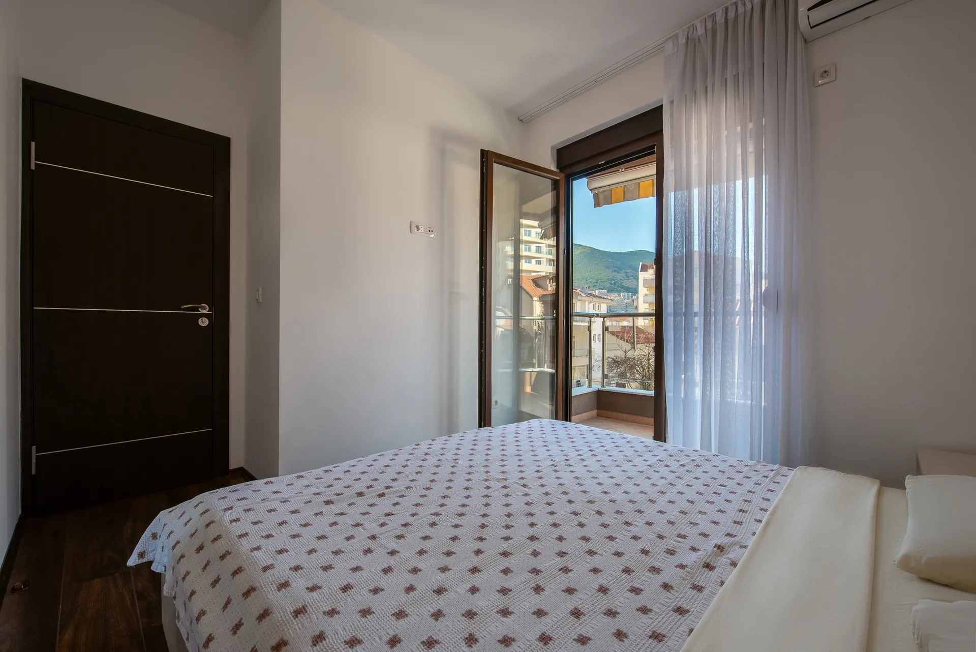 Bedroom featuring a patterned bedspread, dark wood door, and an open balcony overlooking hills.