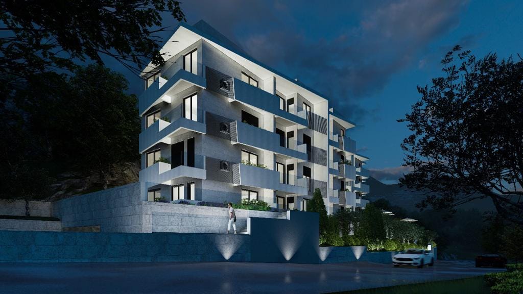 Modern residential complex with facade lighting and balconies in Petrovac, Montenegro, evening view of the building.