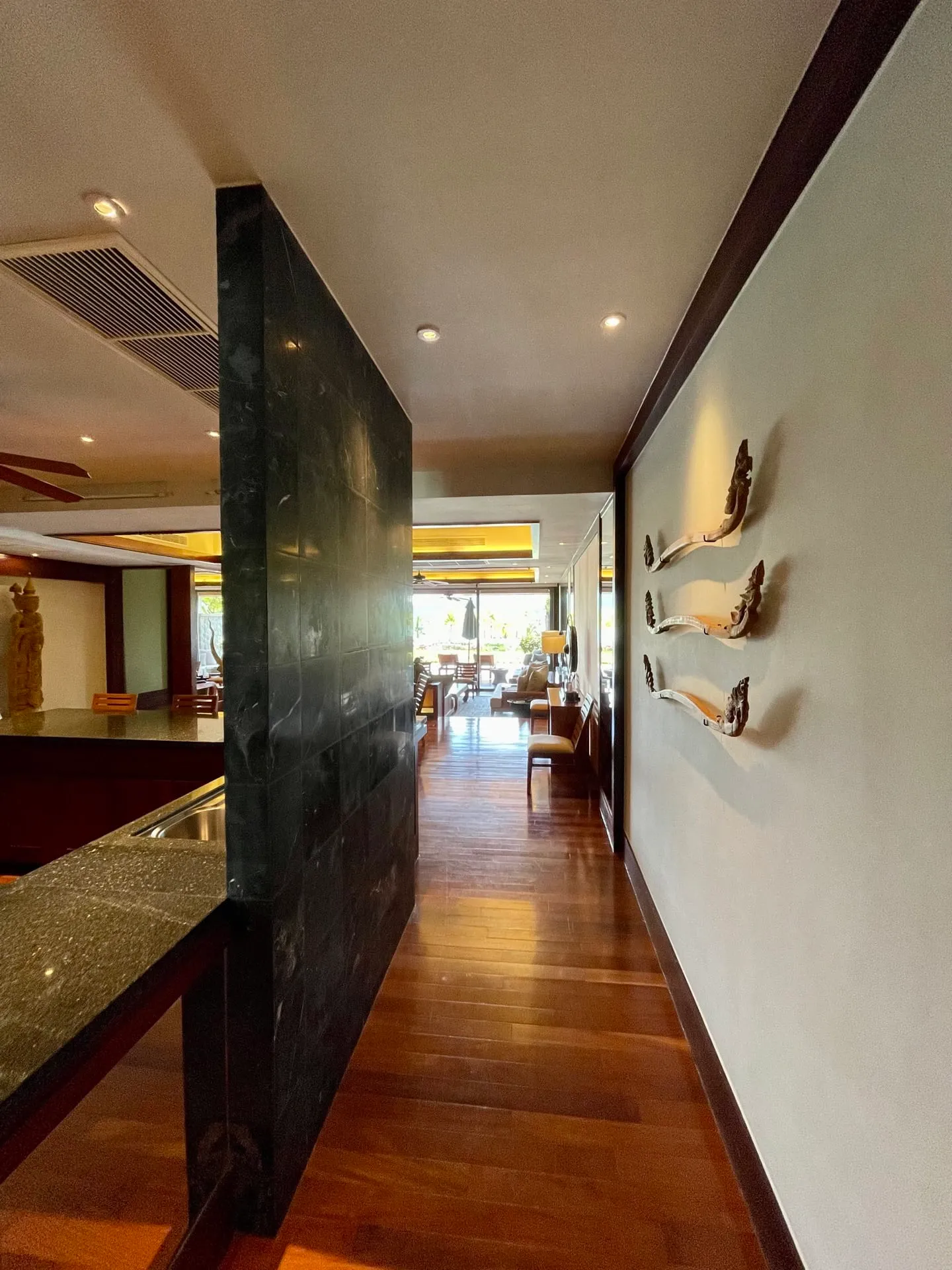 A long hallway with wooden flooring, a dark marble partition wall, and decorative carvings mounted on the light-colored wall to the right.