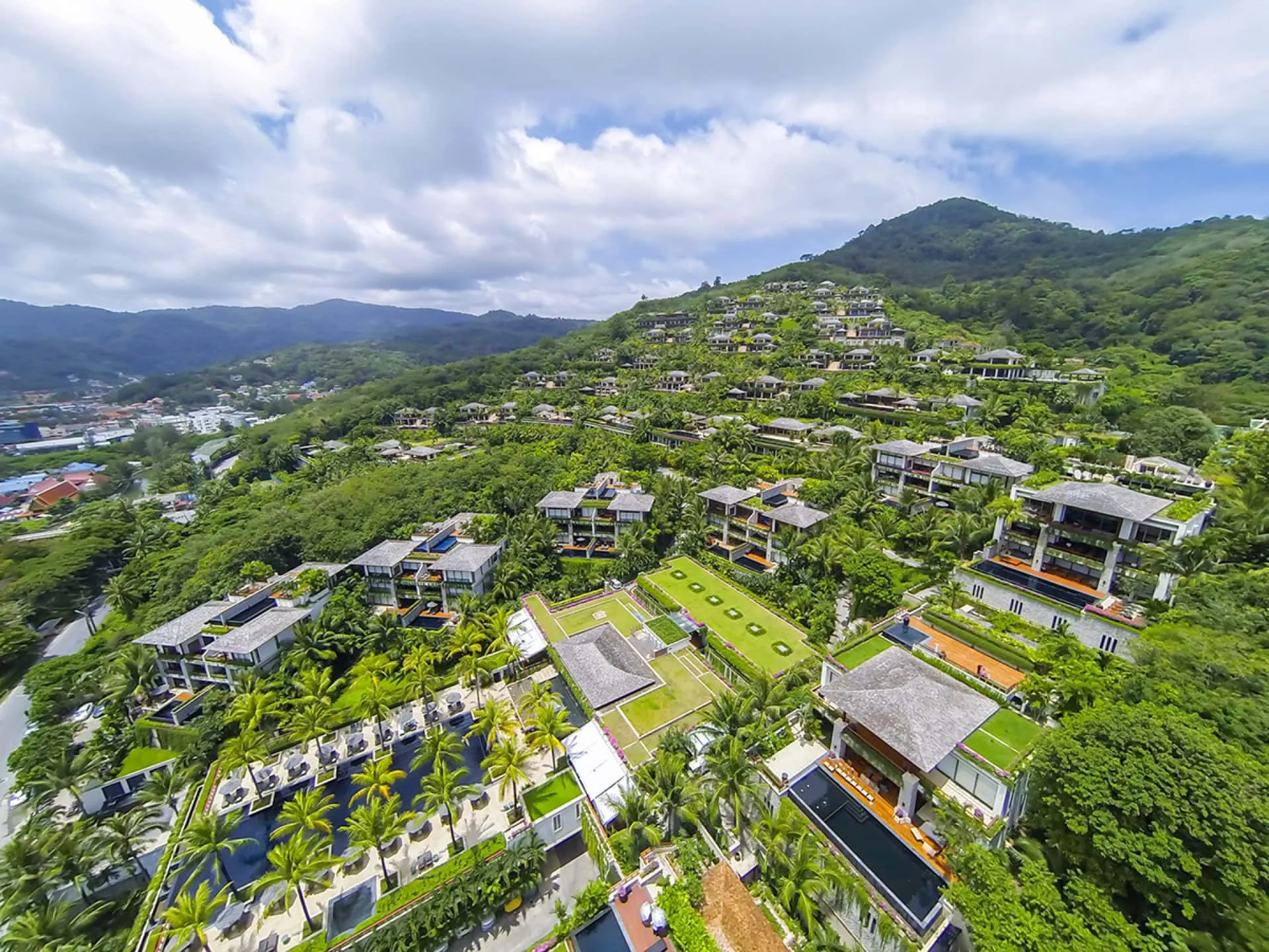 Aerial view of a large hillside resort complex with pools, palm trees, and lush greenery.