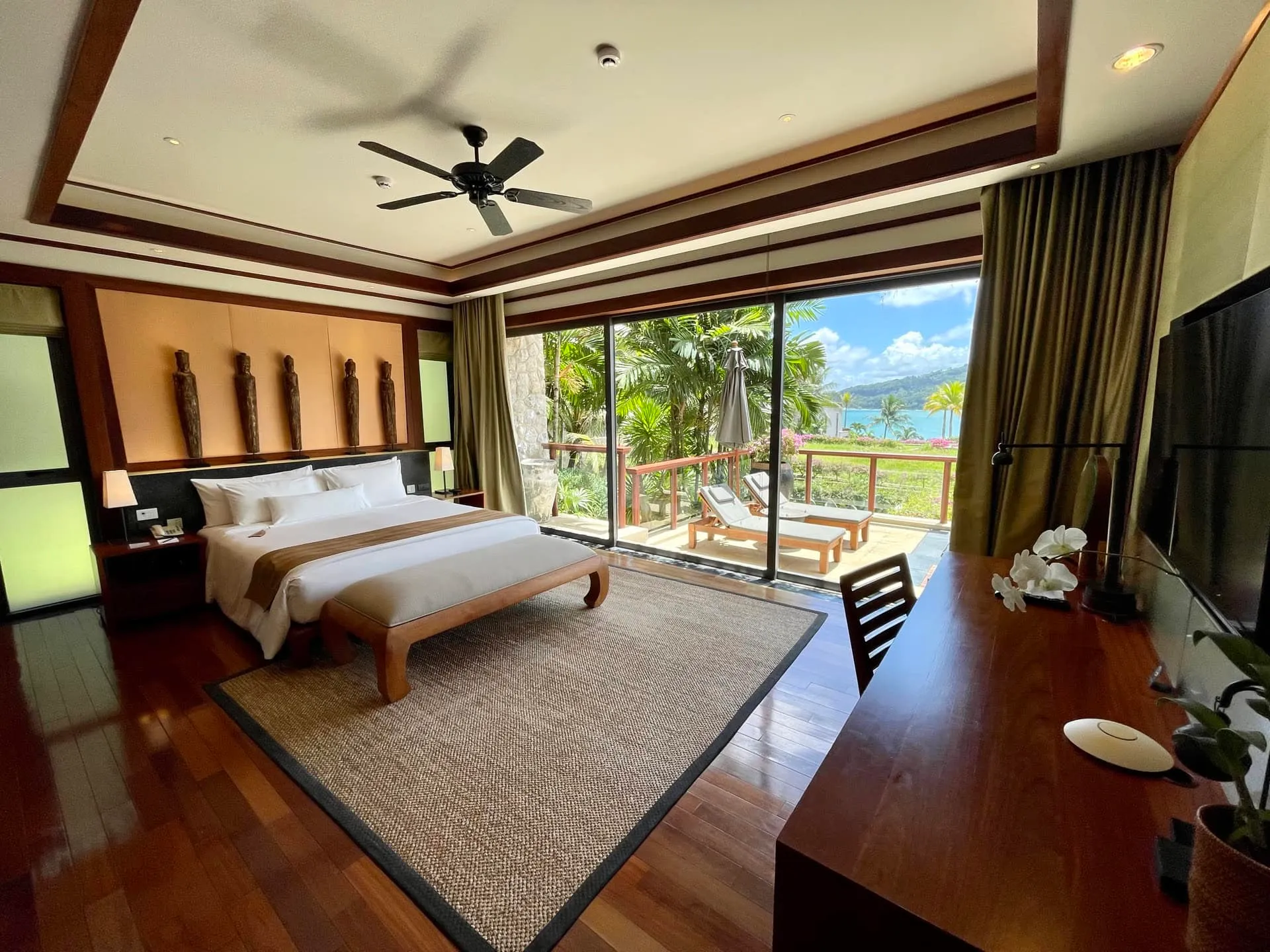 Bedroom featuring a large bed, hardwood floors, ceiling fan, and sliding glass doors leading to an ocean-view balcony.
