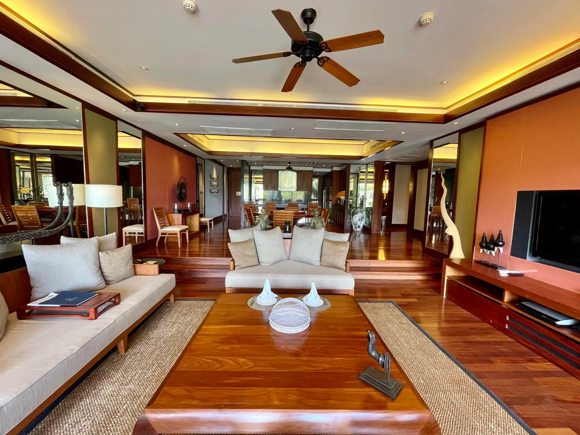 Living room with hardwood floors, beige sofas, a wooden coffee table, and a TV on an orange wall.