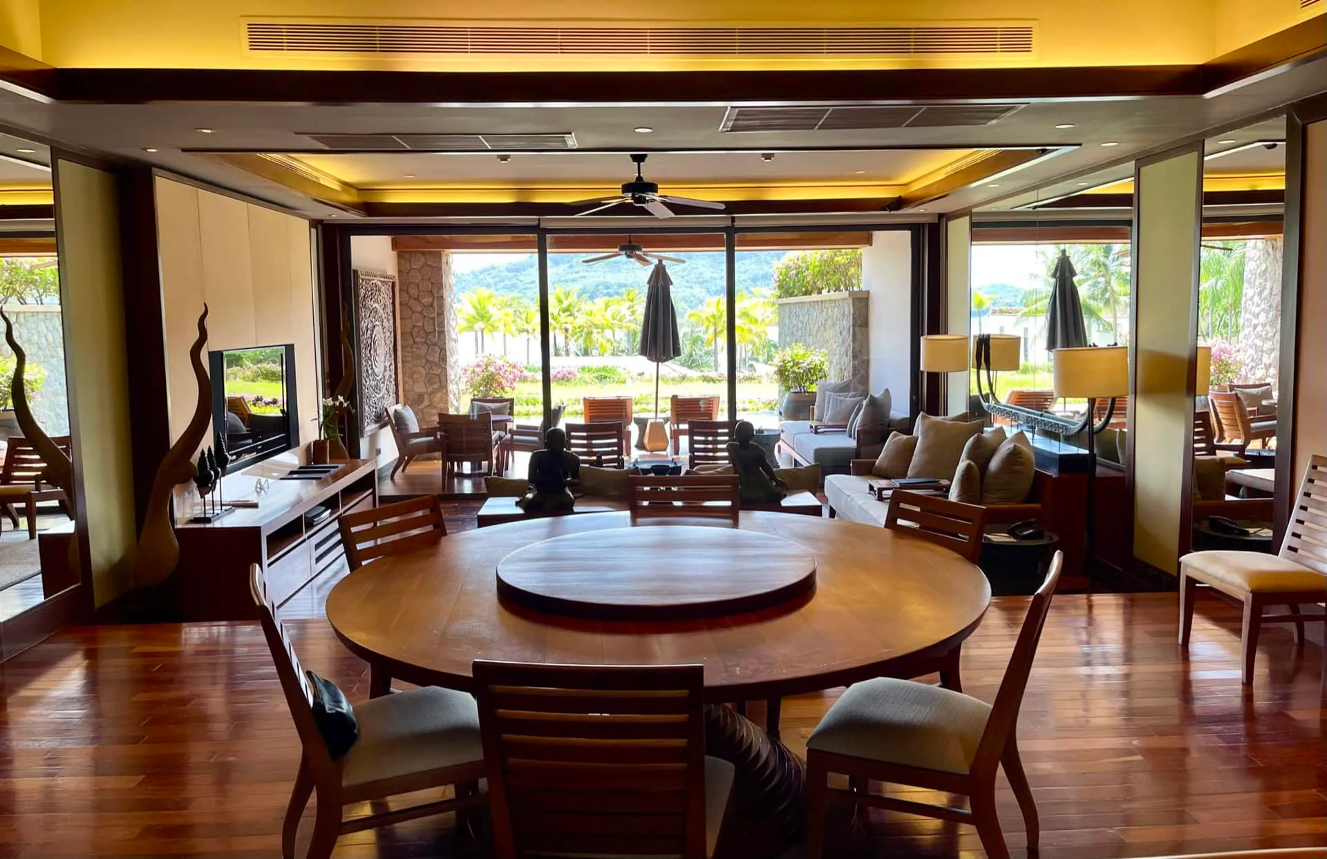 Living room with round wooden dining table, sofa, TV, and large glass doors to garden.
