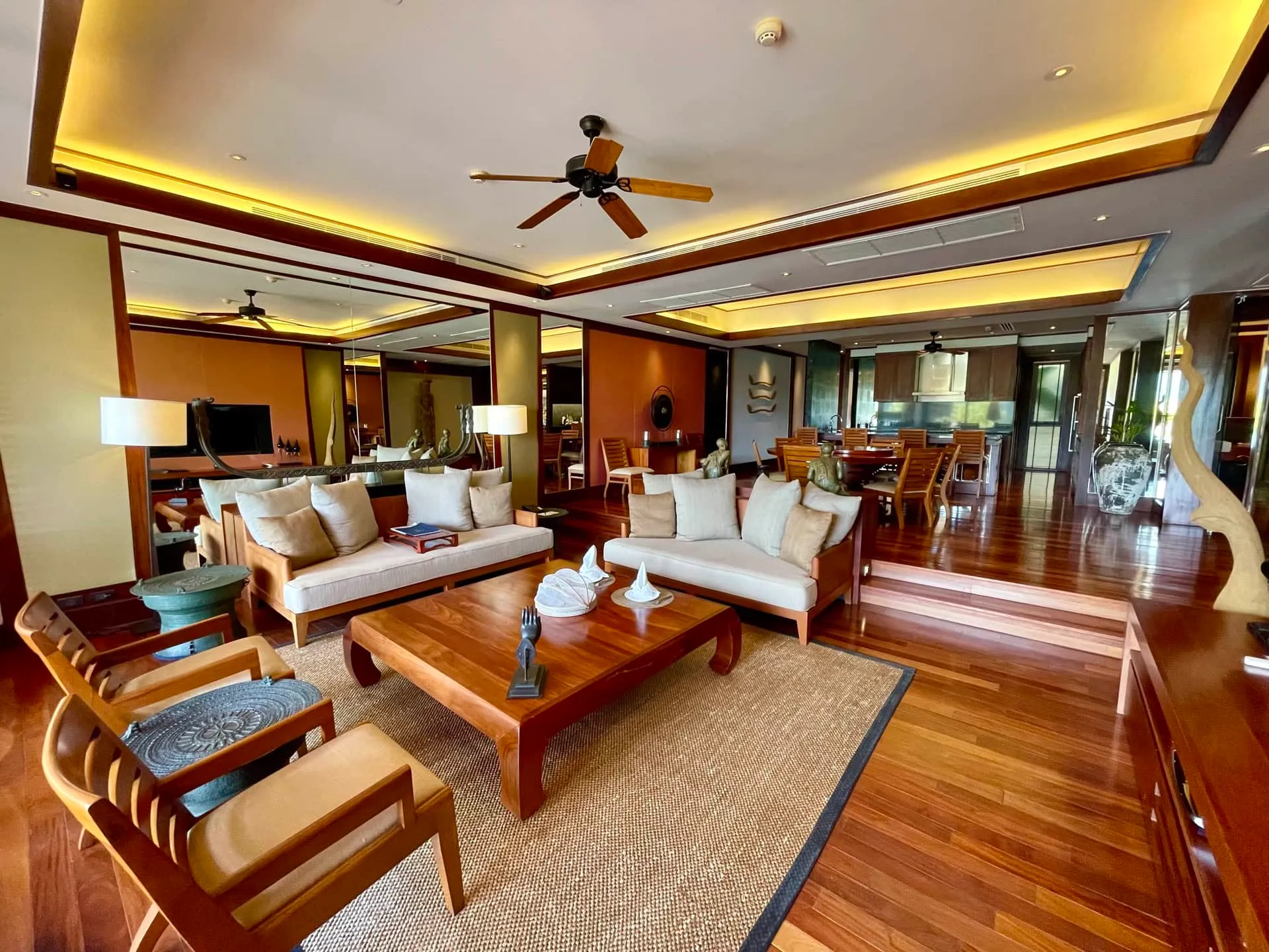 Living room featuring wooden sofas, a coffee table, ceiling fan, and polished hardwood floors with warm ambient lighting.