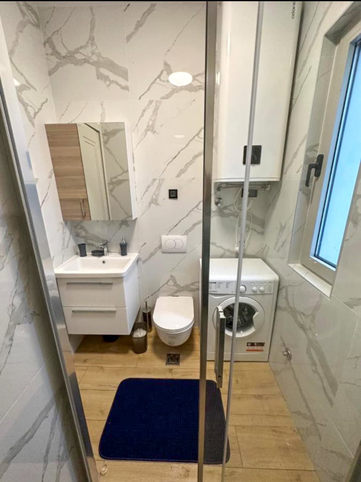 Modern bathroom in an apartment in Budva, Montenegro: marble-look tiles, shower cabin, and washing machine.